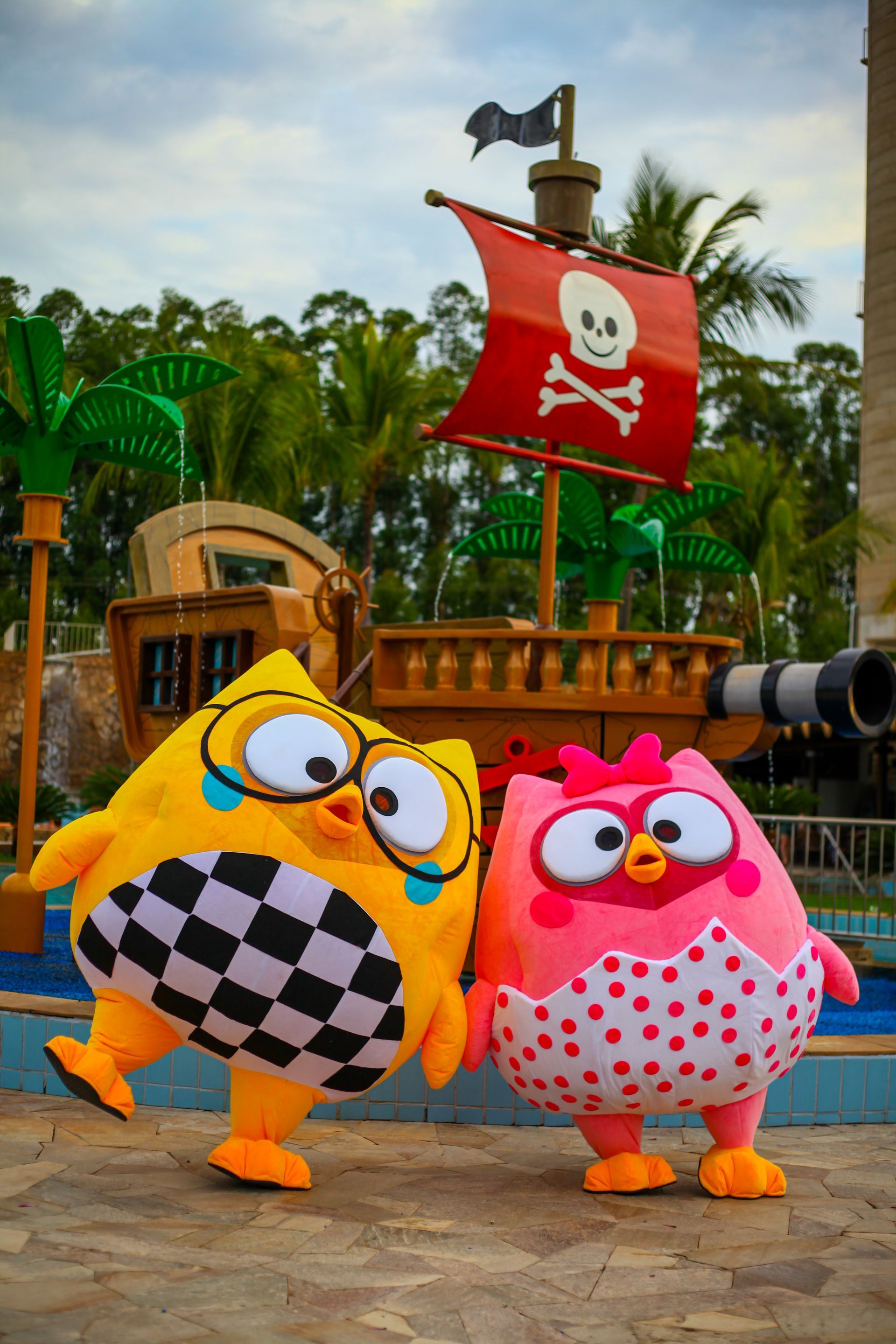 Dois mascotes estão um ao lado do outro em frente a um navio pirata.