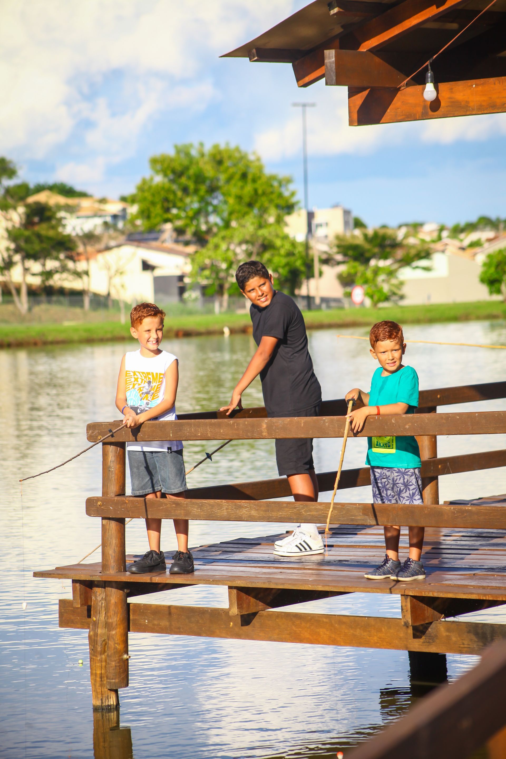 Três meninos estão pescando em um cais de madeira.