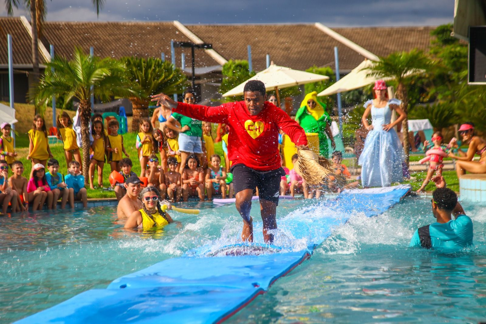 Um homem de camisa vermelha está em uma prancha de surf em uma piscina.