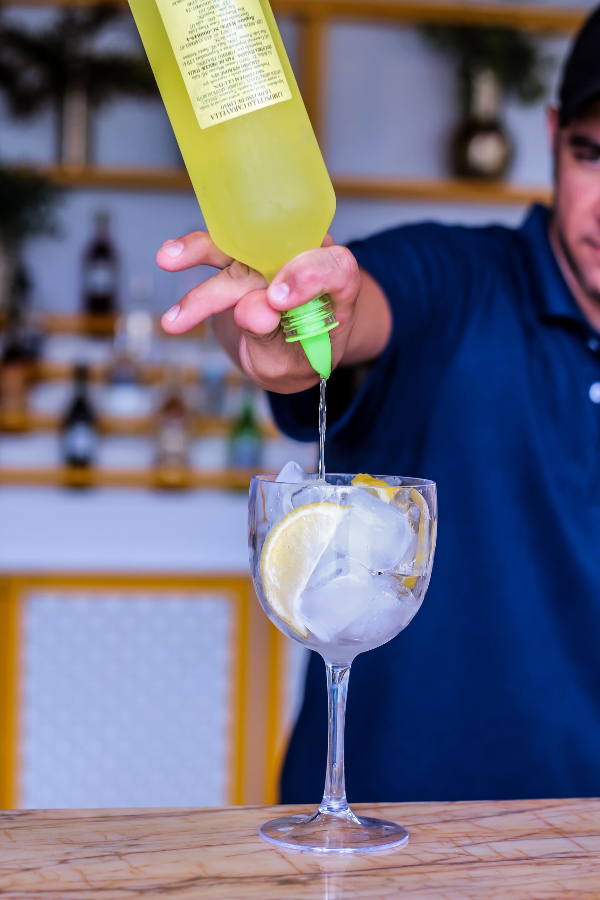 Um barman está servindo uma bebida em um copo com gelo e fatias de limão.