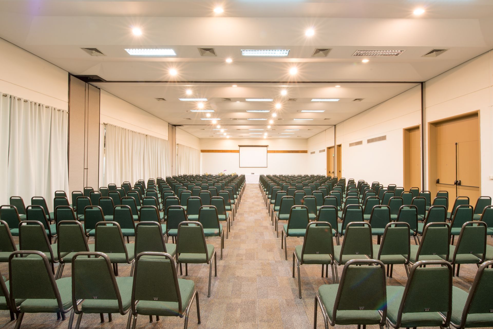 Uma grande sala de conferências com fileiras de cadeiras e uma tela de projetor.