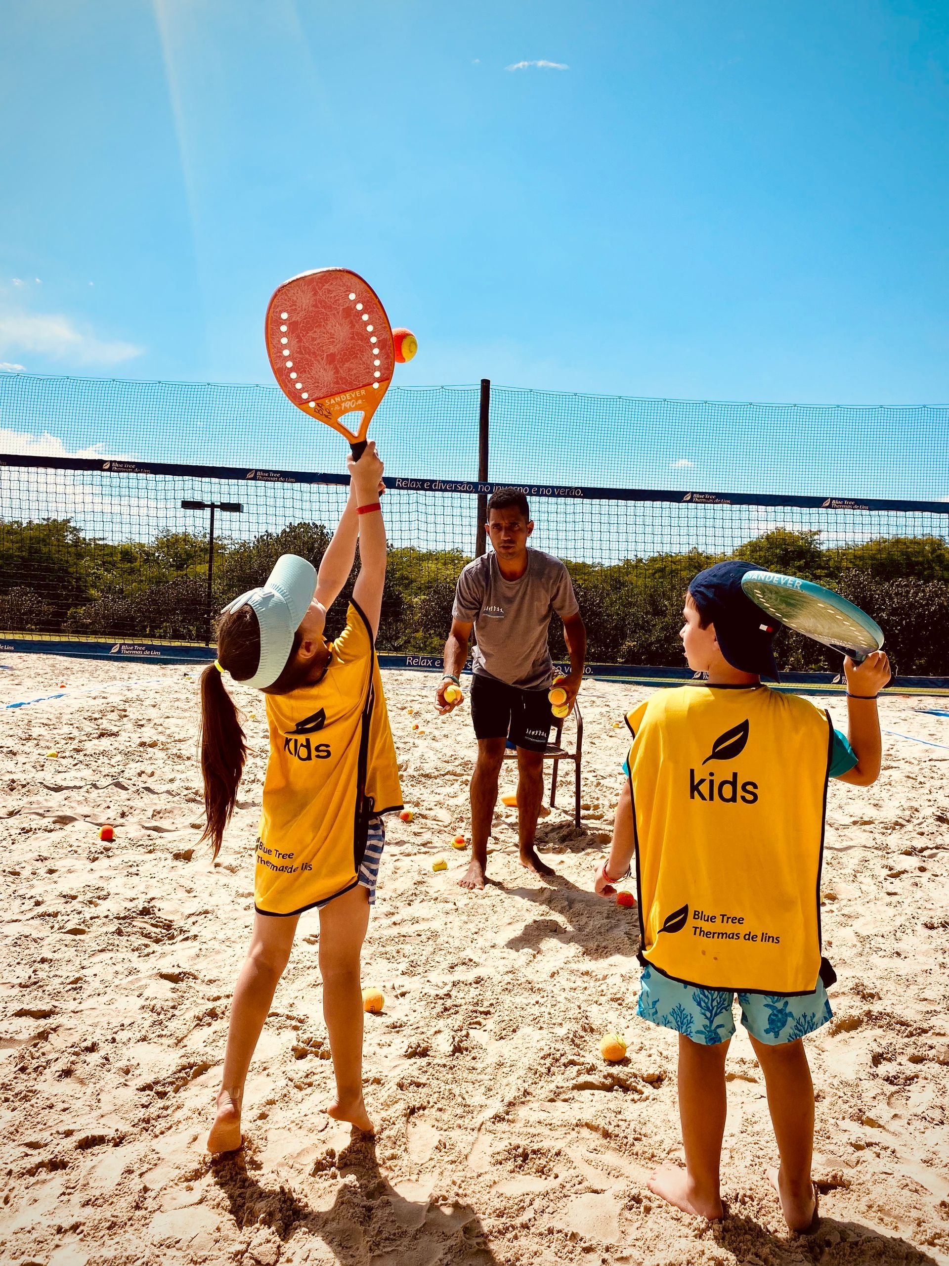 Um grupo de crianças está jogando vôlei em uma praia de areia.