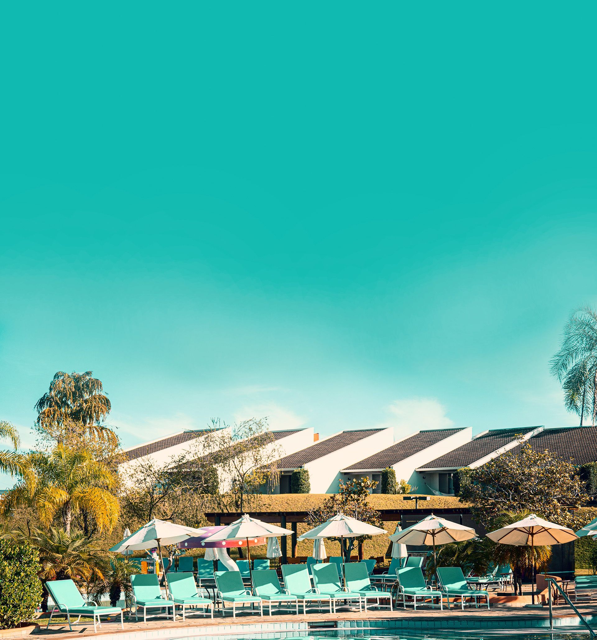 Uma grande piscina cercada por cadeiras e guarda-sóis com um prédio ao fundo.