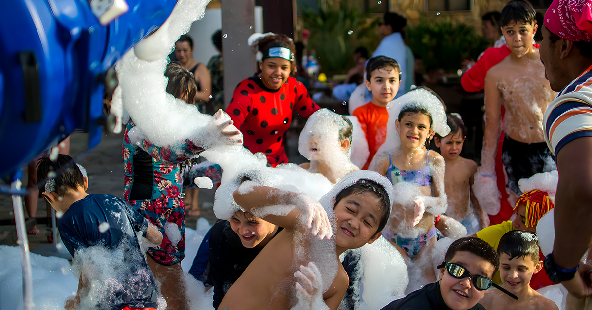 Children playing in a foam-filled crowd, laughing and splashing at an outdoor event