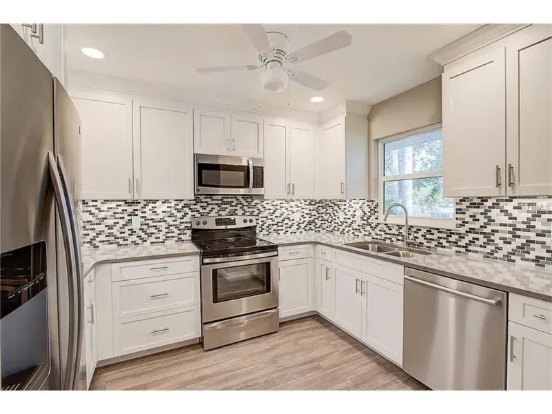 Bright modern kitchen with white cabinets, stainless appliances, mosaic tile backsplash, and a window above the sink