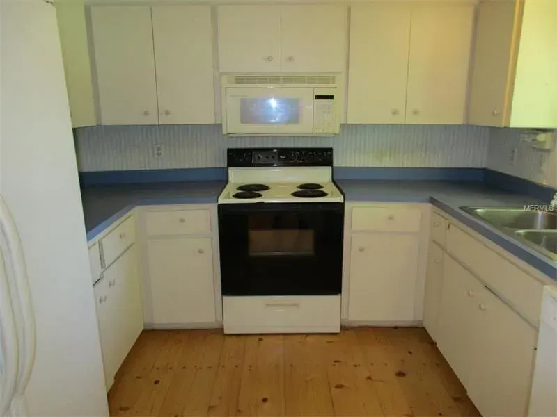 Bright kitchen with white cabinets, black stove, and light wood floor