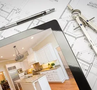 Tablet showing a kitchen design over architectural plans with a pencil and compass on the desk