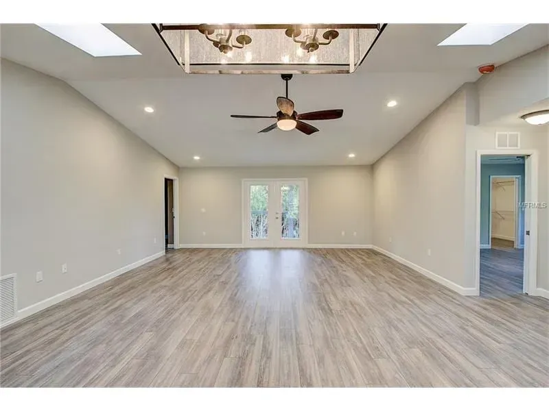 Spacious empty living room with wood-look floors, ceiling fans, recessed lights, and double glass doors.