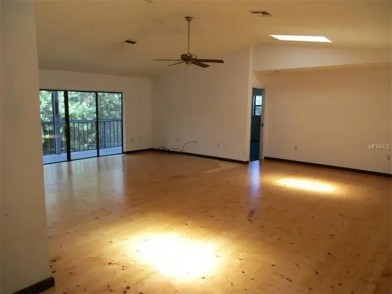 Empty living room with wood floors, ceiling fan, and sliding glass doors to a patio