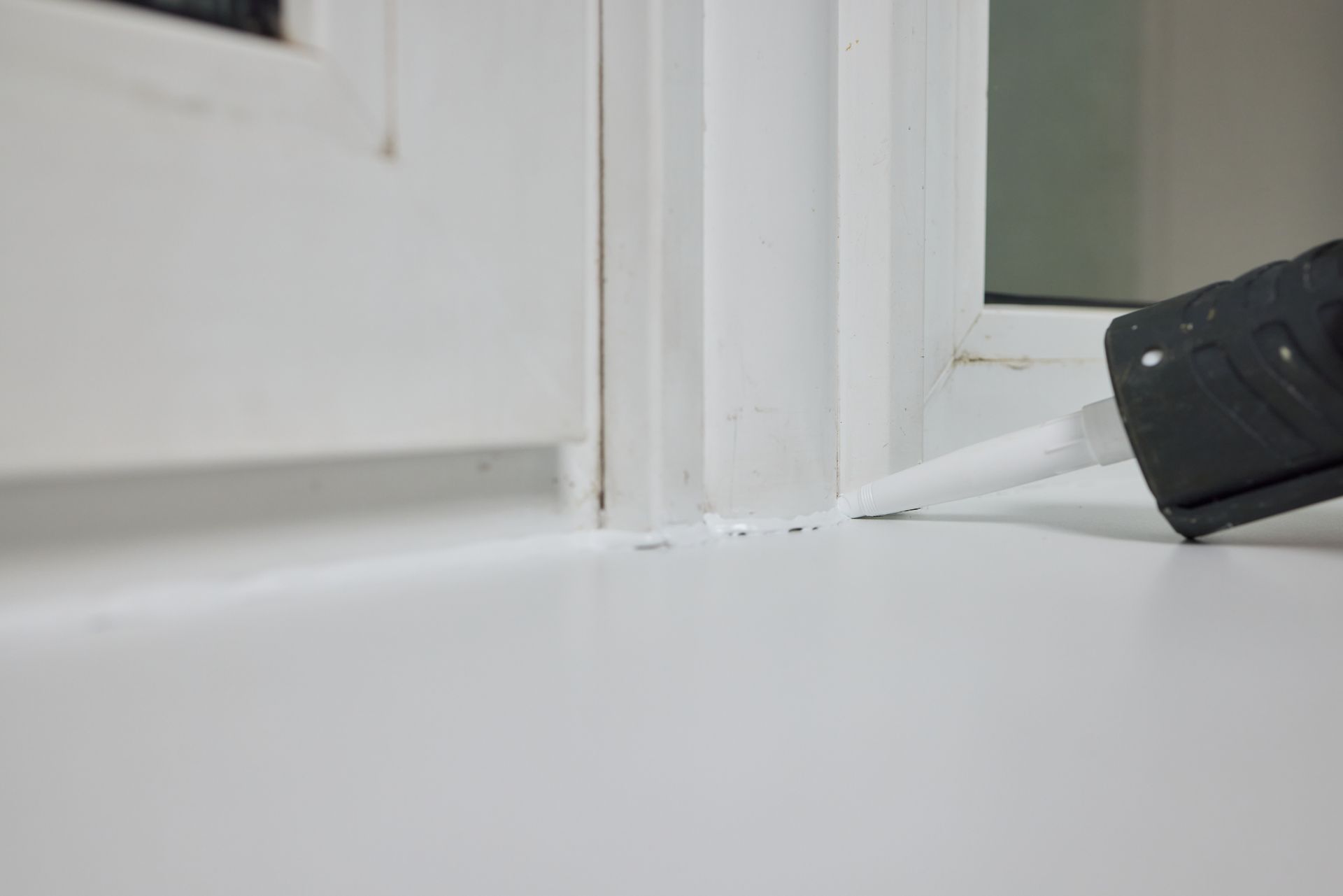 Caulk gun applying sealant along a white window frame and sill Caulk gun applying sealant along a white window frame and sill