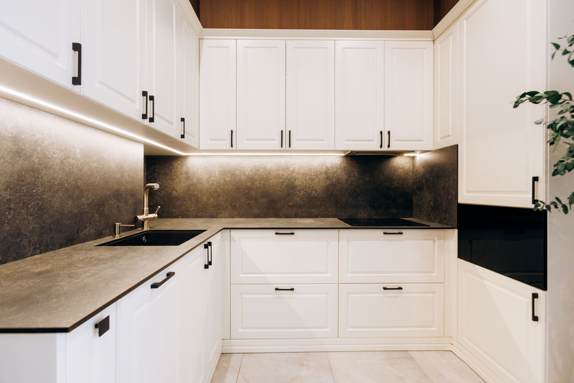 Modern white kitchen with black countertops, under-cabinet lighting, and built-in appliances.
