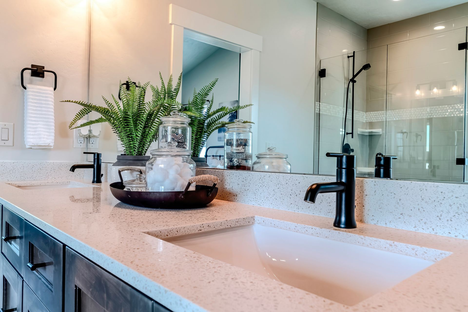 Modern bathroom vanity with white countertop, black faucet, sink, and vase of flowers near a glass shower Modern bathroom vanity with white countertop, black faucet, sink, and vase of flowers near a glass shower