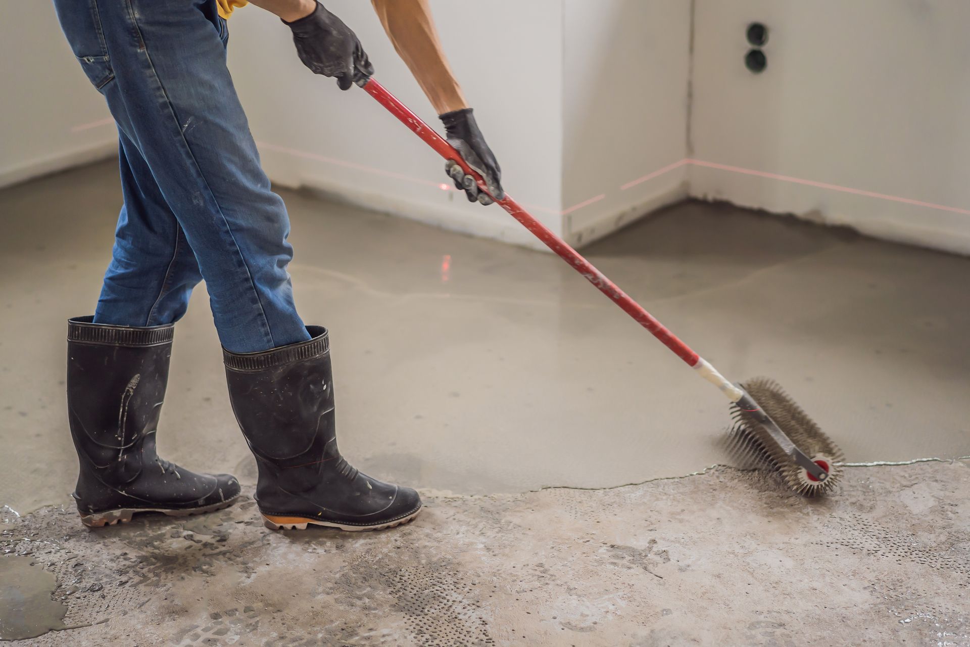 Worker sweeping debris from a concrete floor with a red push broom indoors Worker sweeping debris from a concrete floor with a red push broom indoors