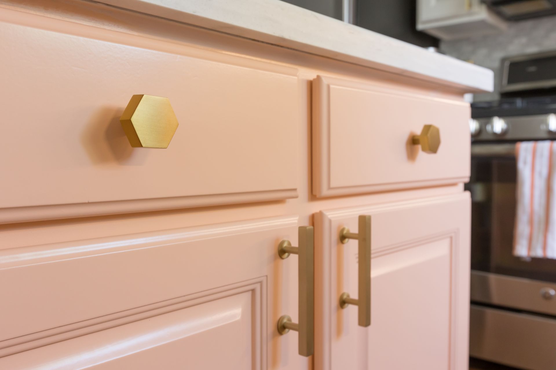 Close-up of cream kitchen cabinets with gold hexagonal and bar handles. Close-up of cream kitchen cabinets with gold hexagonal and bar handles.