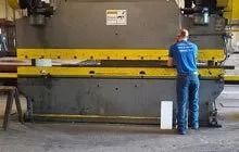 Worker inspecting a large industrial machine in a factory, with yellow safety bars.