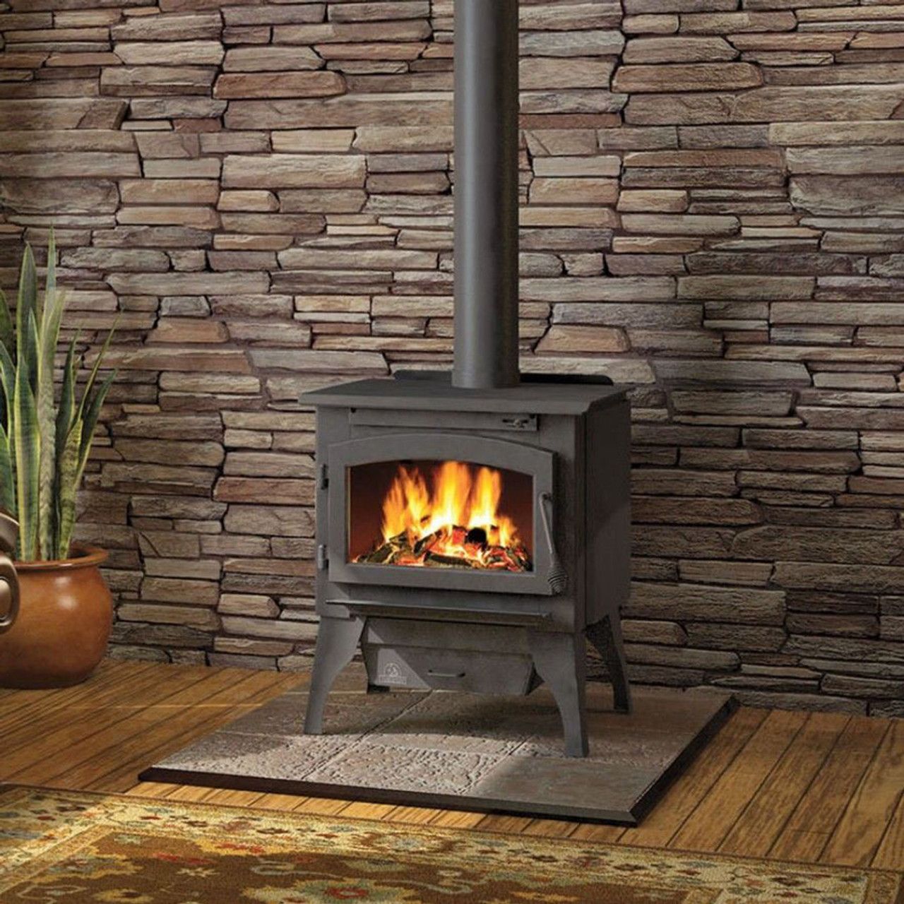 A wood stove is lit up in front of a stone wall
