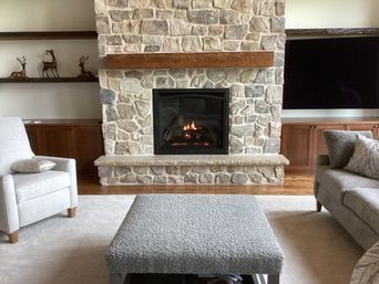 Living room with stone fireplace, wooden mantle, and built-in shelves/cabinets. Furniture includes a chair, sofa, and ottoman.