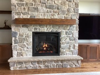 Fireplace with stone facade, wooden mantel, lit fire, and built-in cabinets.