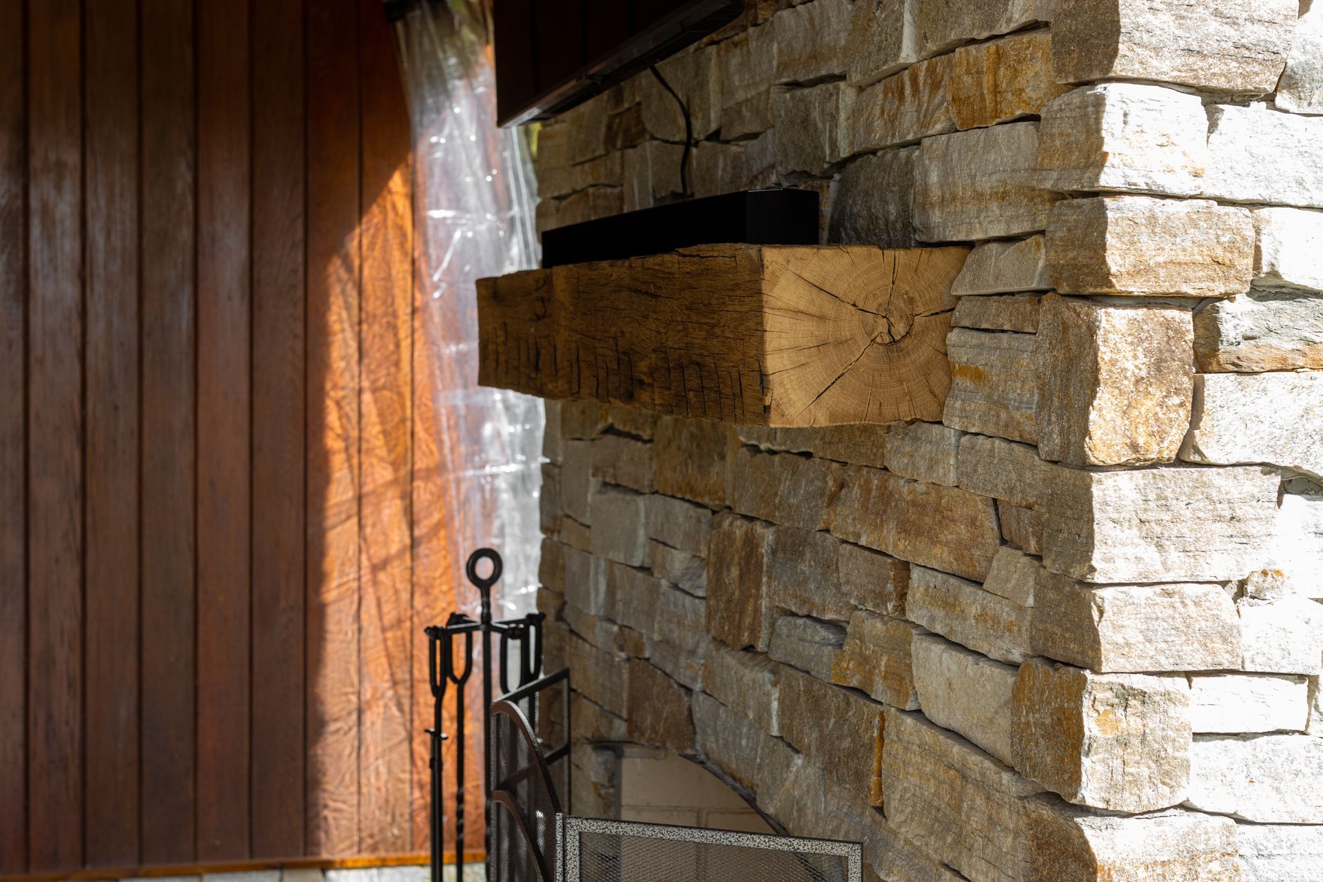 A stone fireplace with a wooden mantle on the side of a house.