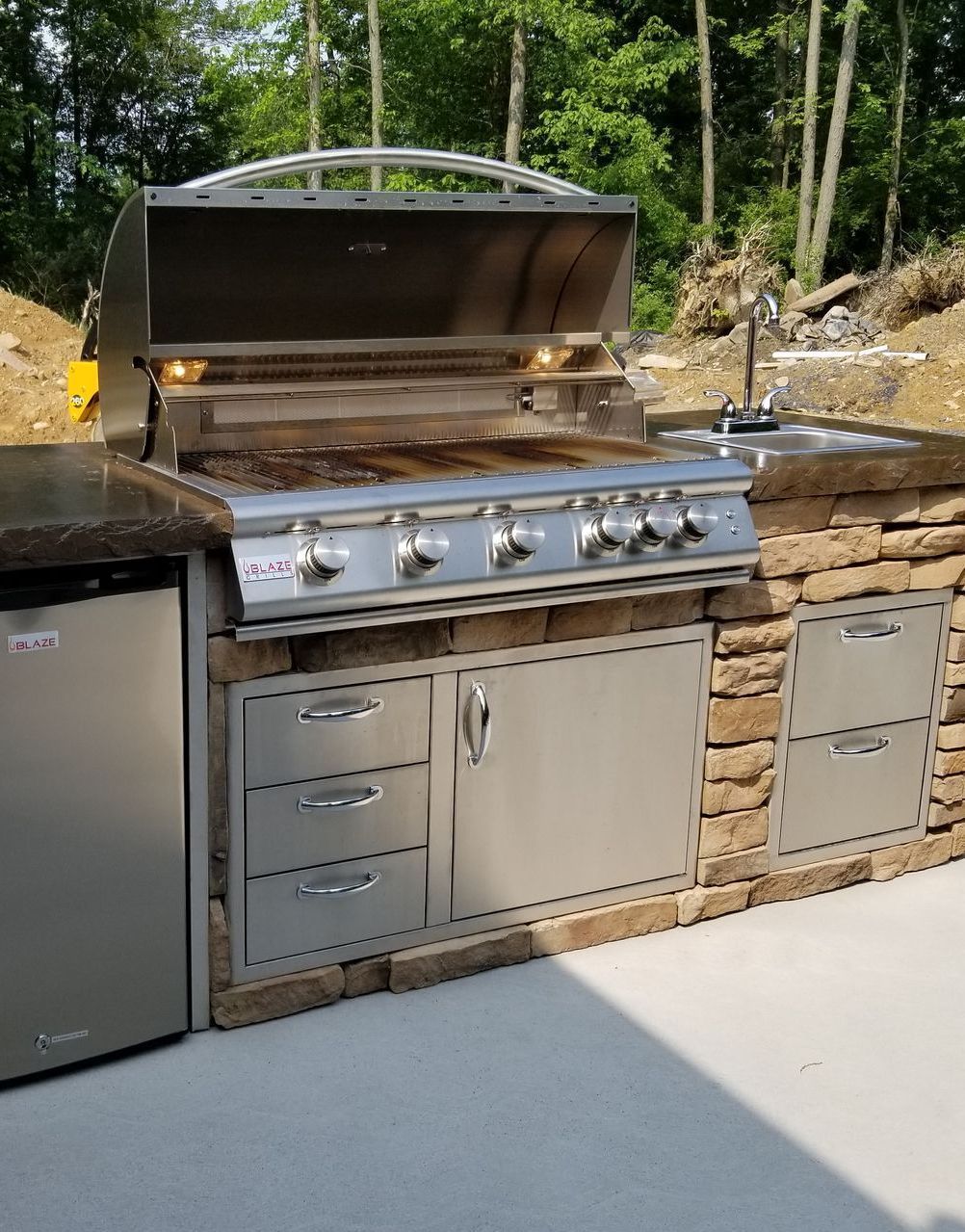 An outdoor kitchen with a stainless steel grill and a stainless steel refrigerator