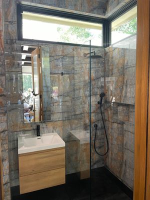 Modern bathroom with glass shower, wall-mounted sink, black floor, and stone tile walls