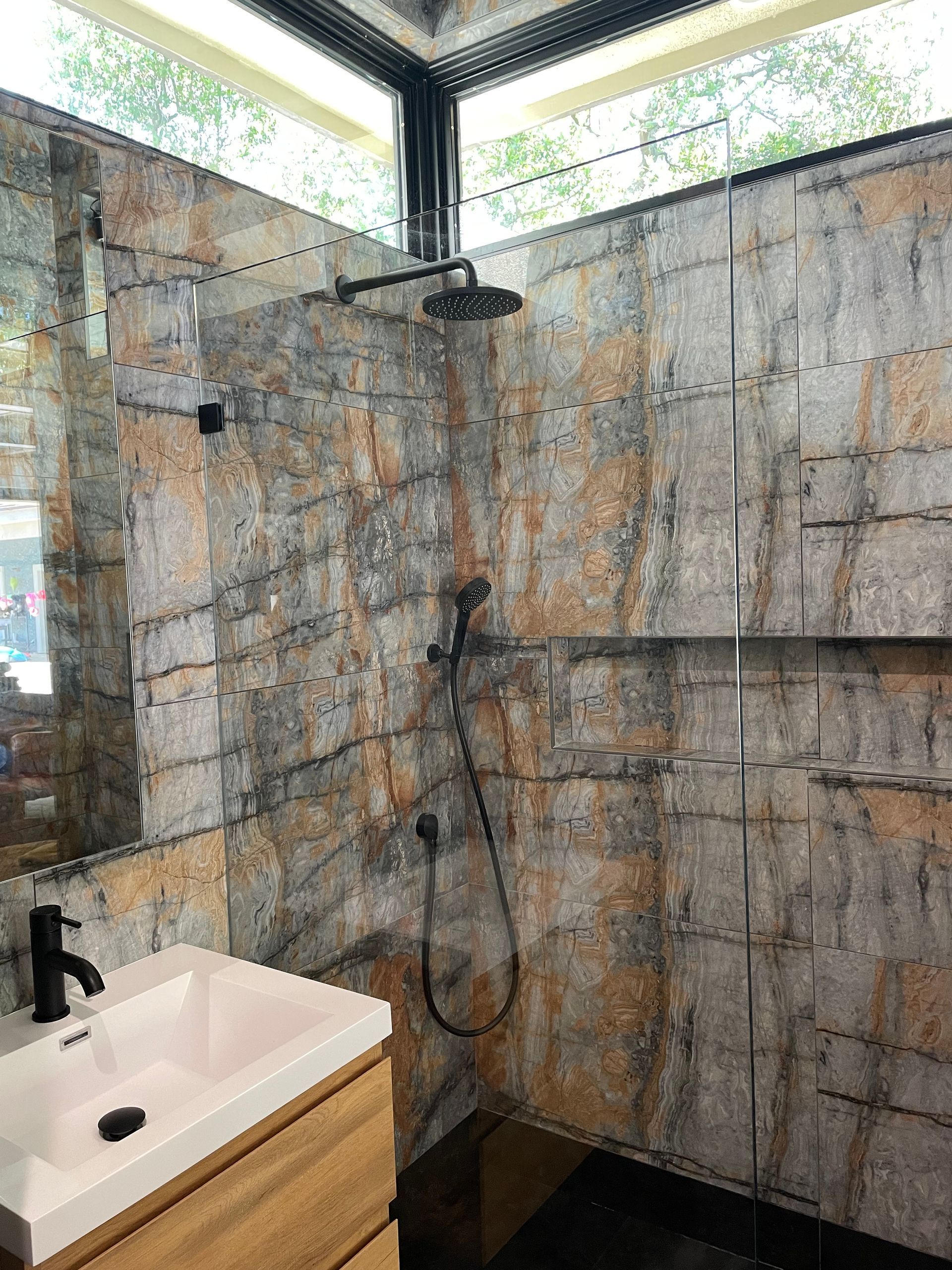 Modern shower and sink in a tiled bathroom with black fixtures and frosted window panels