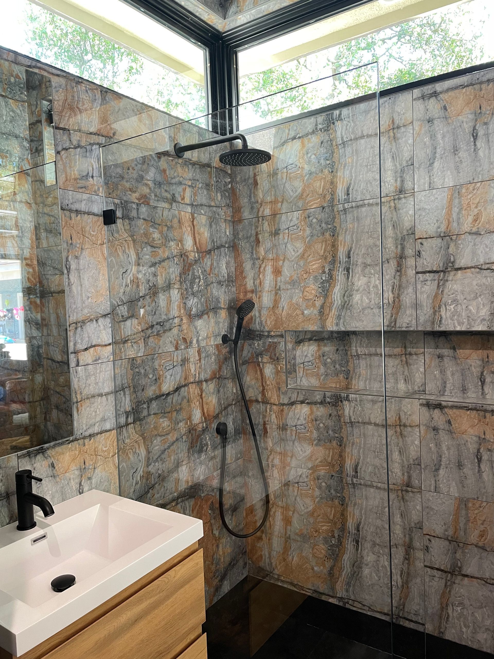 Modern shower with stone-pattern tile walls, black fixtures, and a pink sink in the corner.