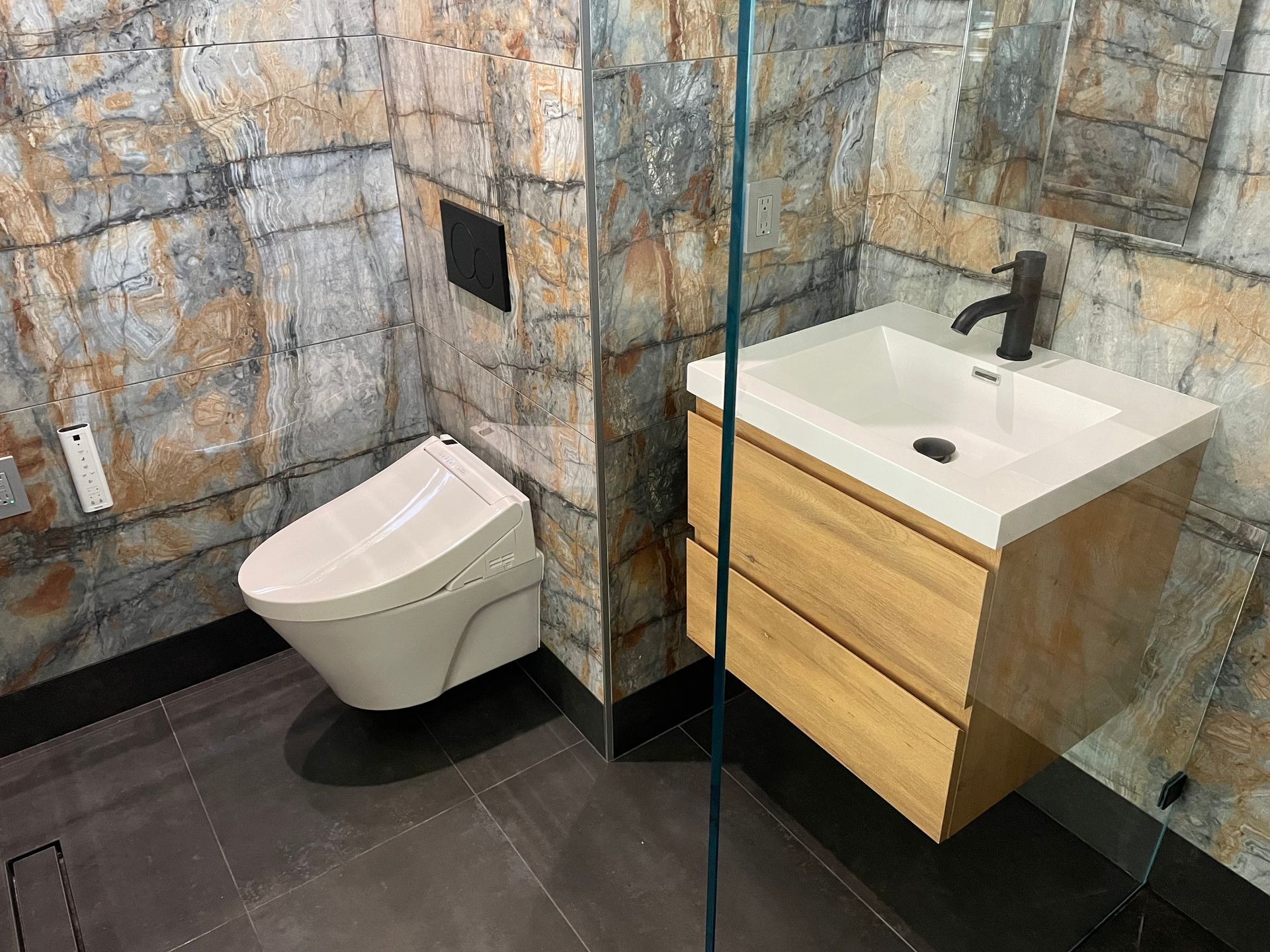 Modern bathroom with wall-mounted toilet, sink vanity, stone tiles, and glass shower partition