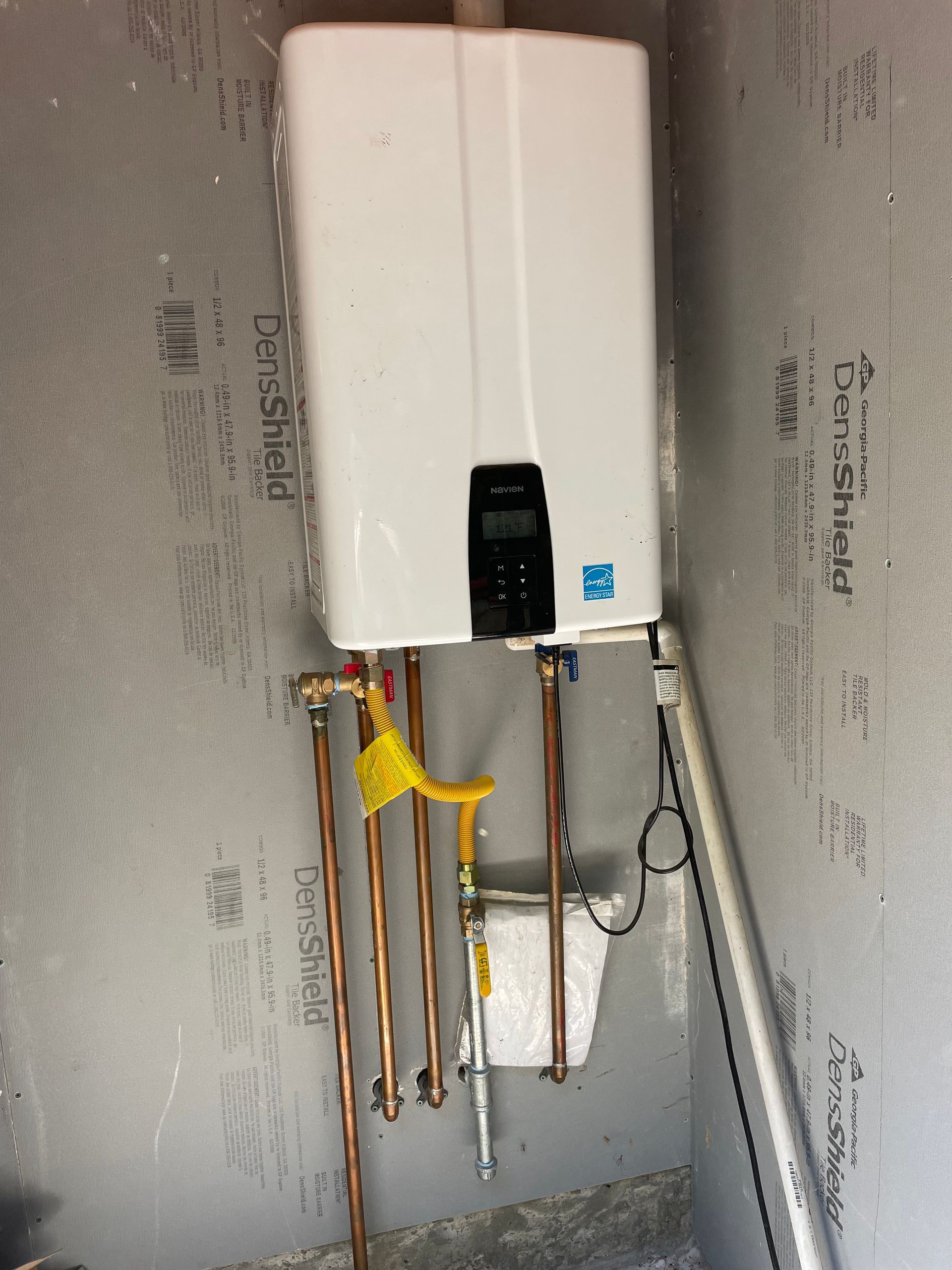 White wall-mounted air conditioner with exposed copper pipes and a hose on a gray wall