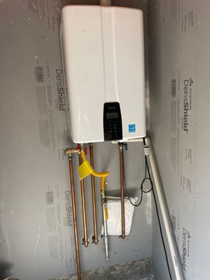 White wall-mounted air conditioner with exposed copper pipes and a hose on a gray wall