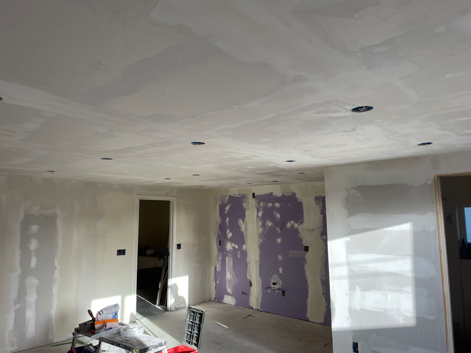 Partially renovated room with drywall patches, exposed ceiling lights, and a window covered in plastic