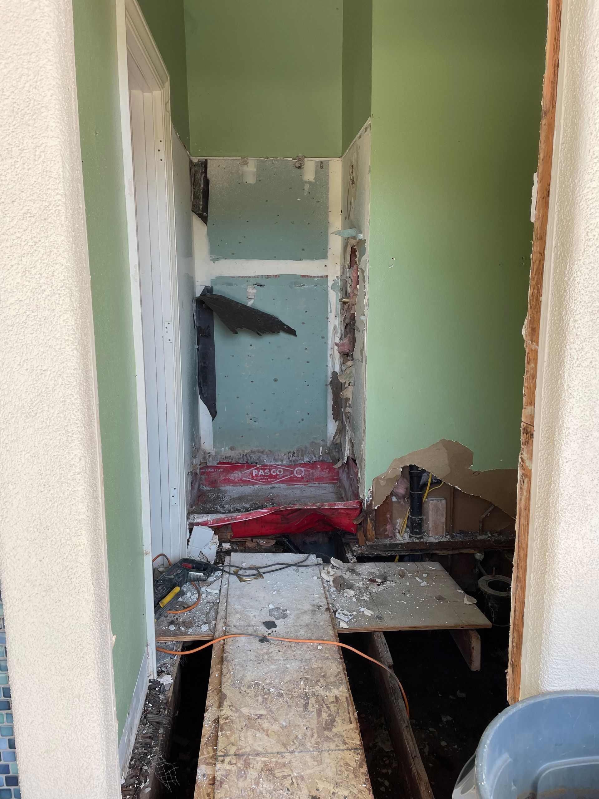 Narrow damaged hallway with exposed floor beams, debris, and peeling green walls.