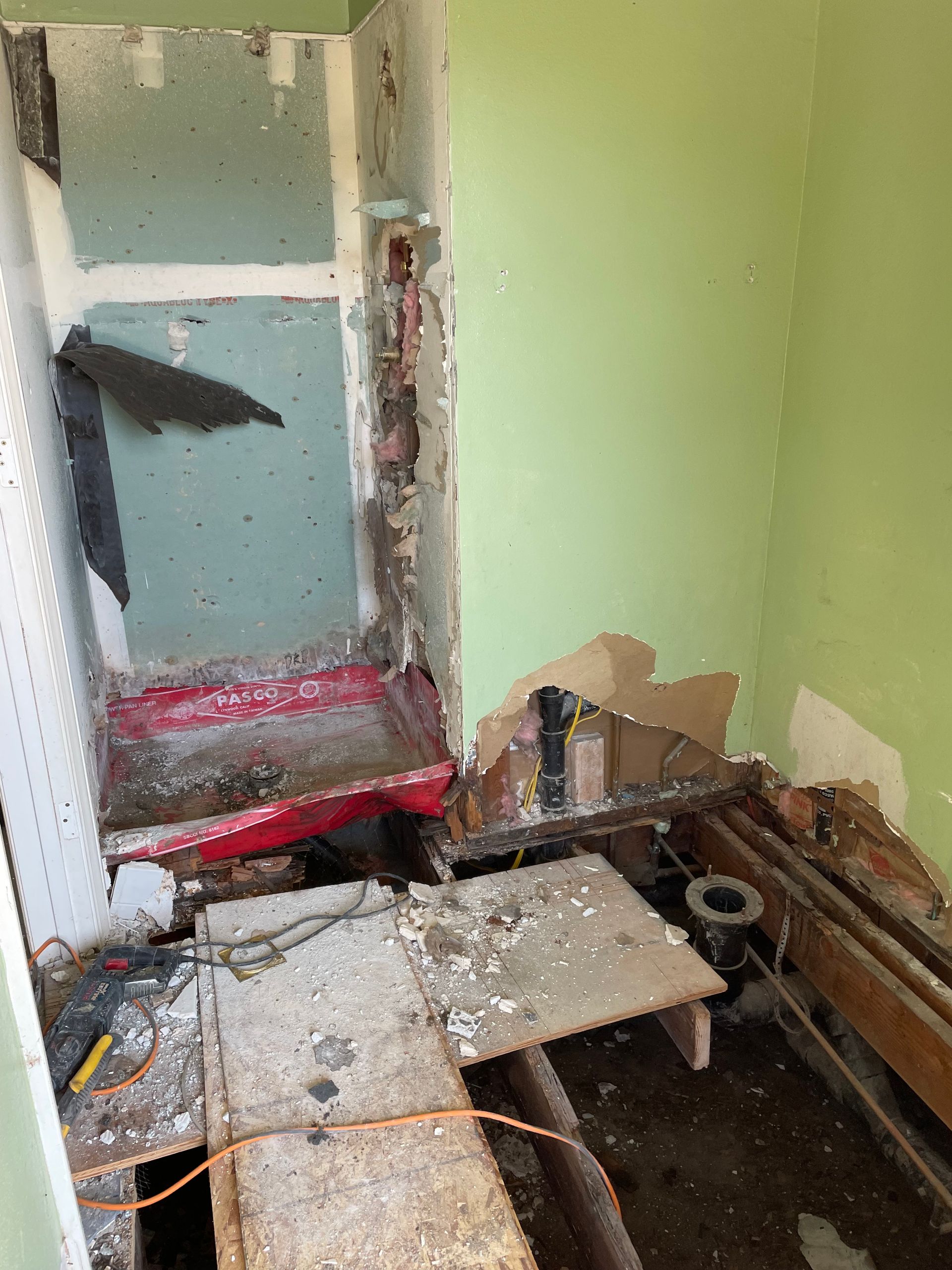 Damaged room with debris, broken floor, and peeling green walls near a doorway