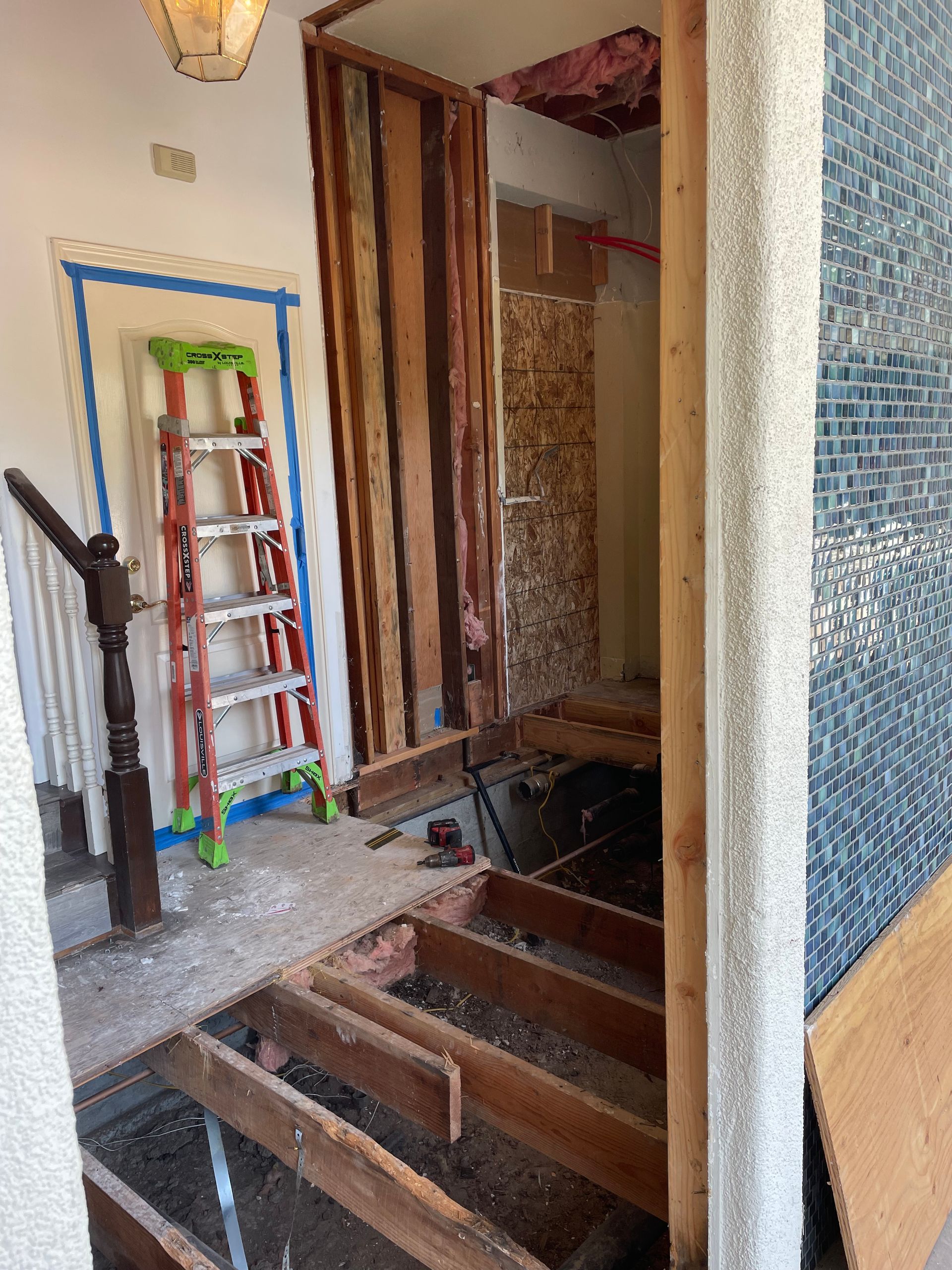 Renovation site with open floor boards, ladder, and tiled walls in a hallway