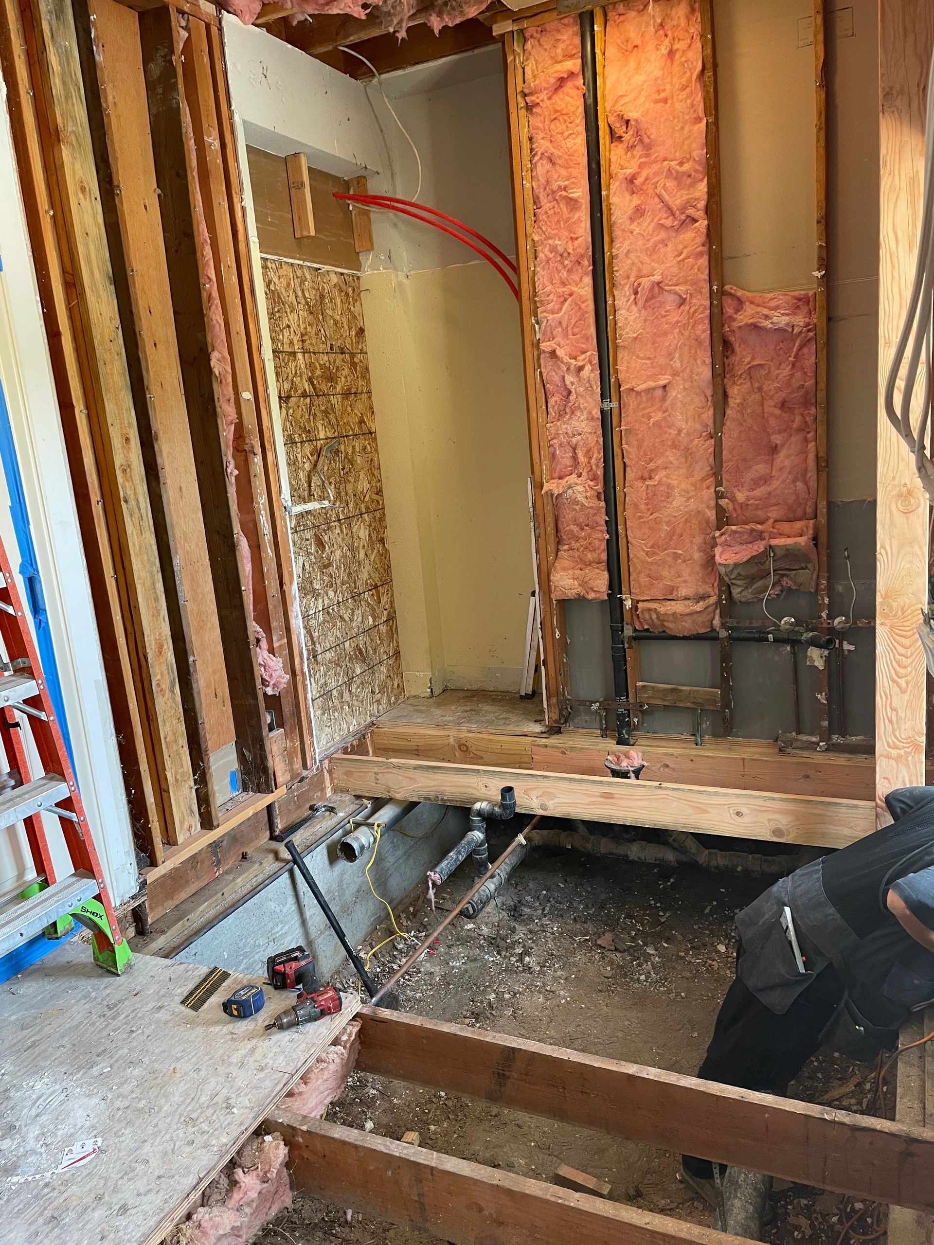 Open wall under renovation with exposed studs, insulation, wiring, and construction debris on the floor