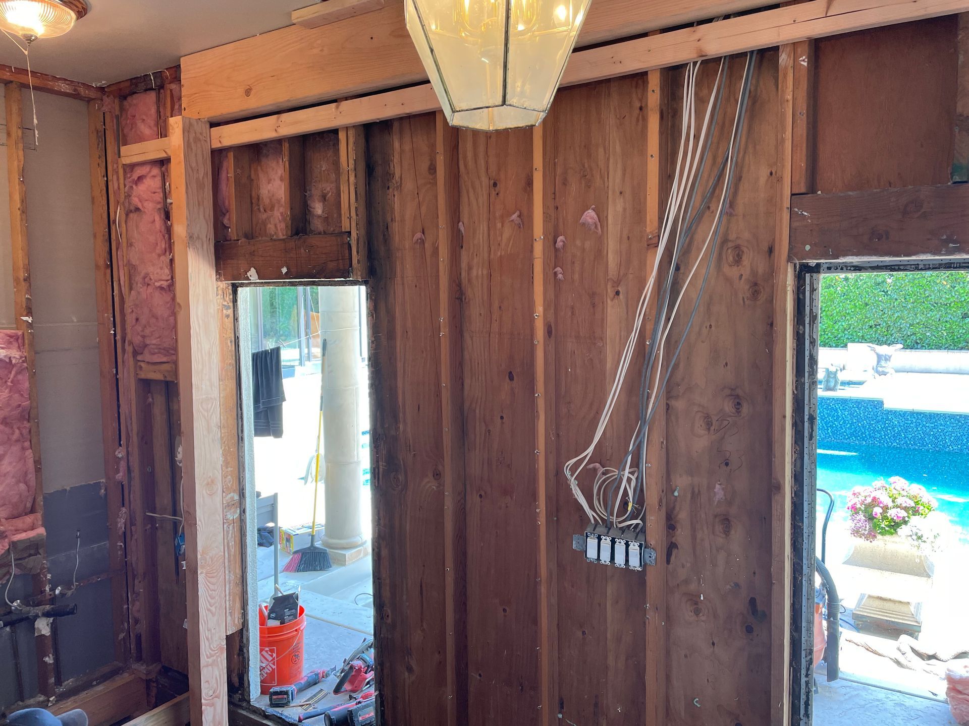 Wood-paneled room with exposed wiring, a hanging light fixture, and an open doorway to a bright outdoor area.