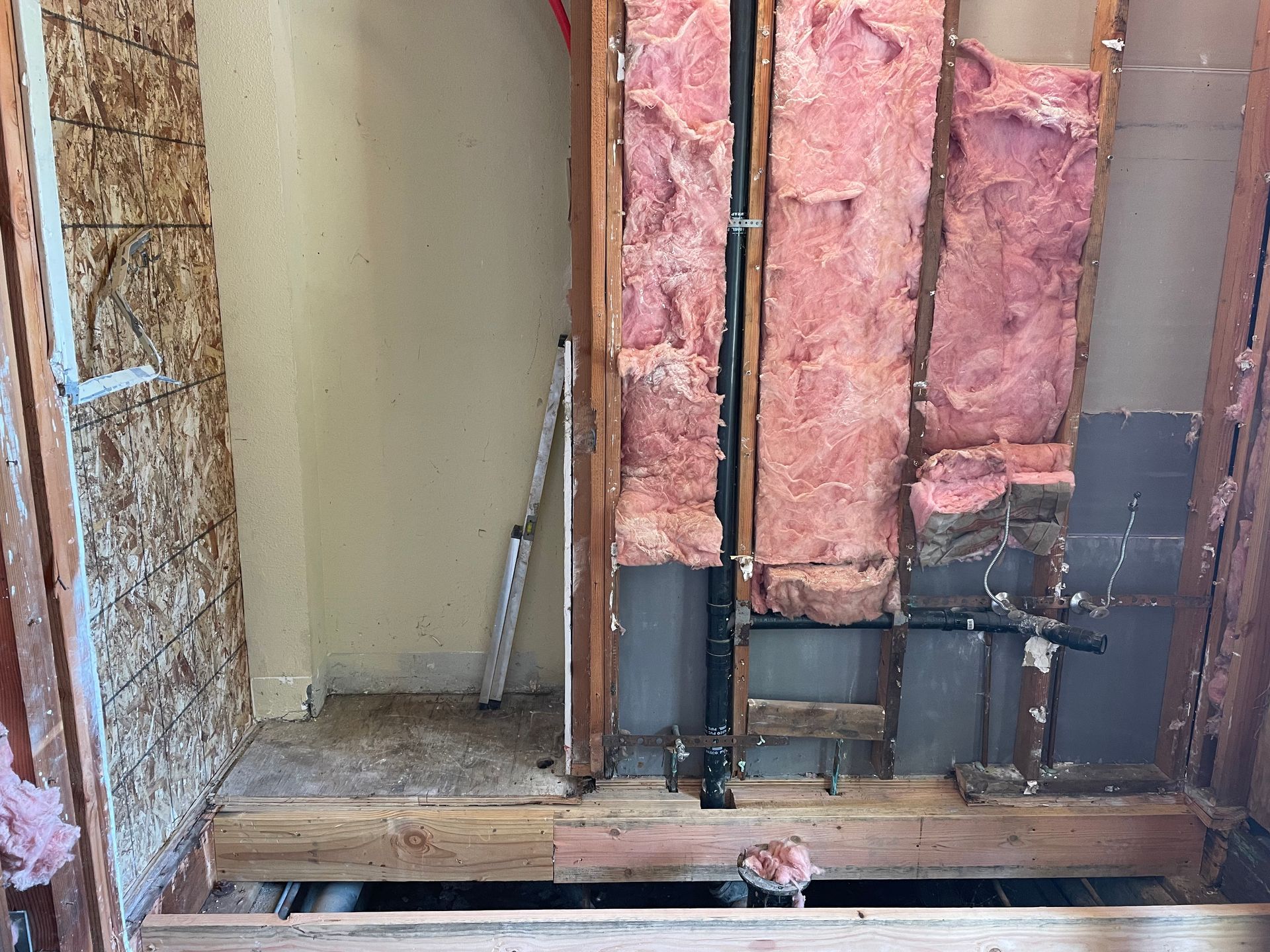 Partially demolished interior wall with exposed insulation, framing, and debris on the floor