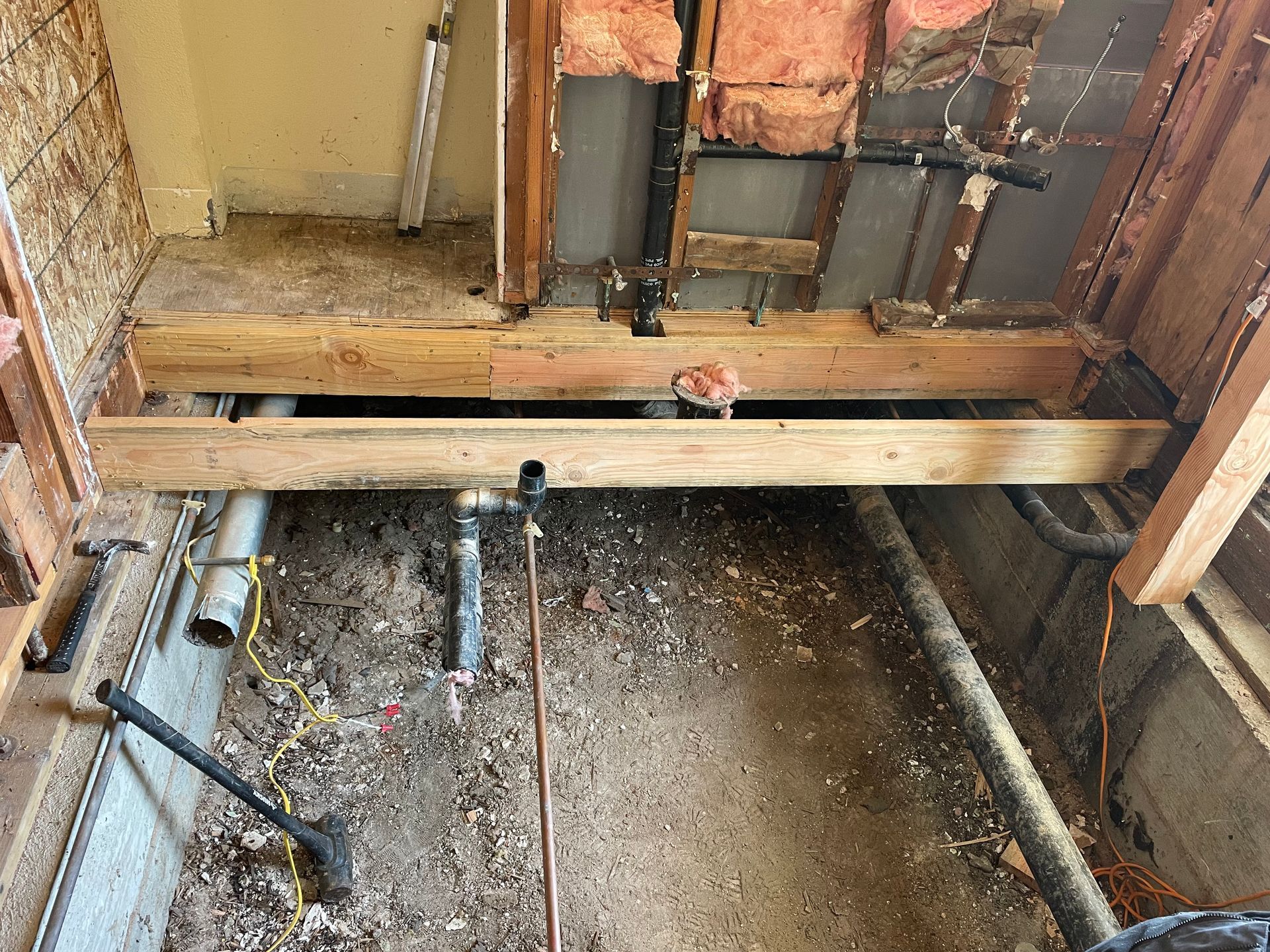 Partially demolished bathroom floor with exposed joists, pipes, and debris