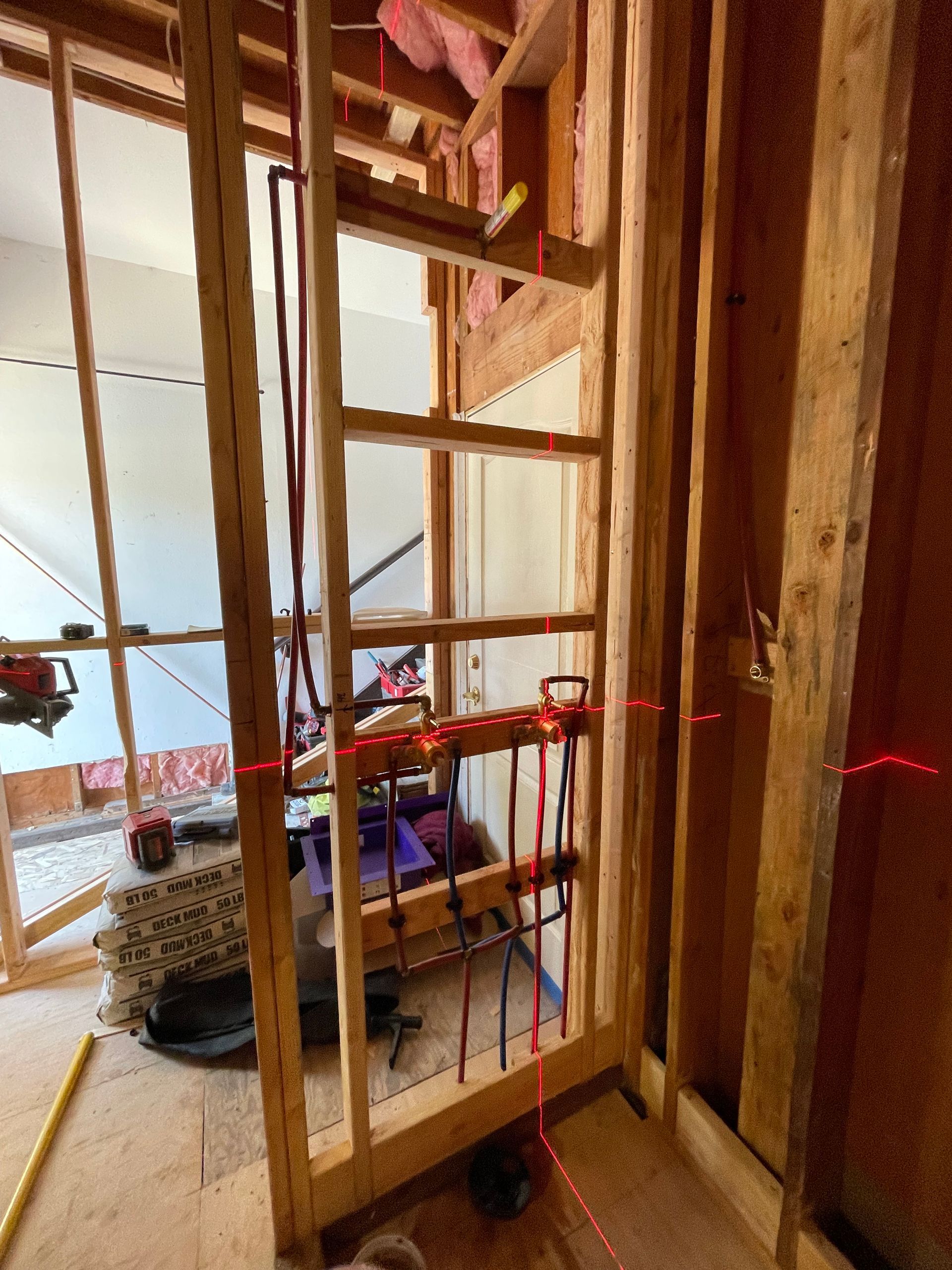 Wood-framed interior under construction with exposed studs, tools, and a person working in the background