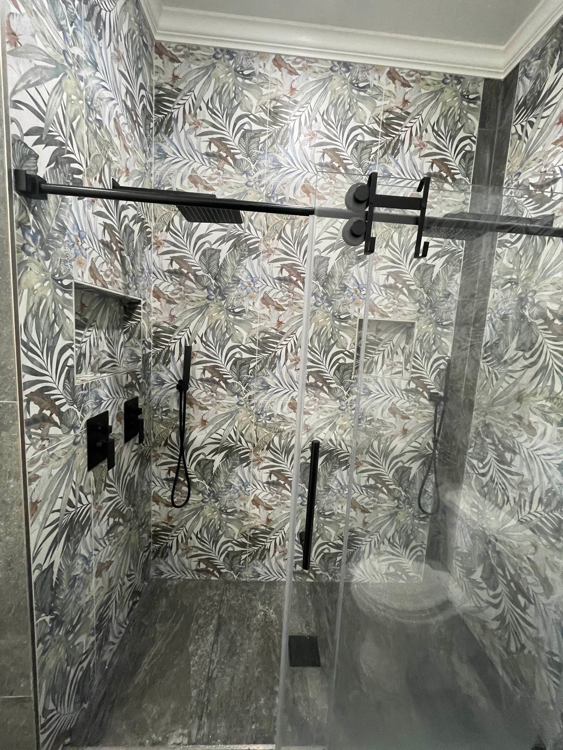 Patterned shower room with black grab bars and a handheld shower on a gray tiled floor