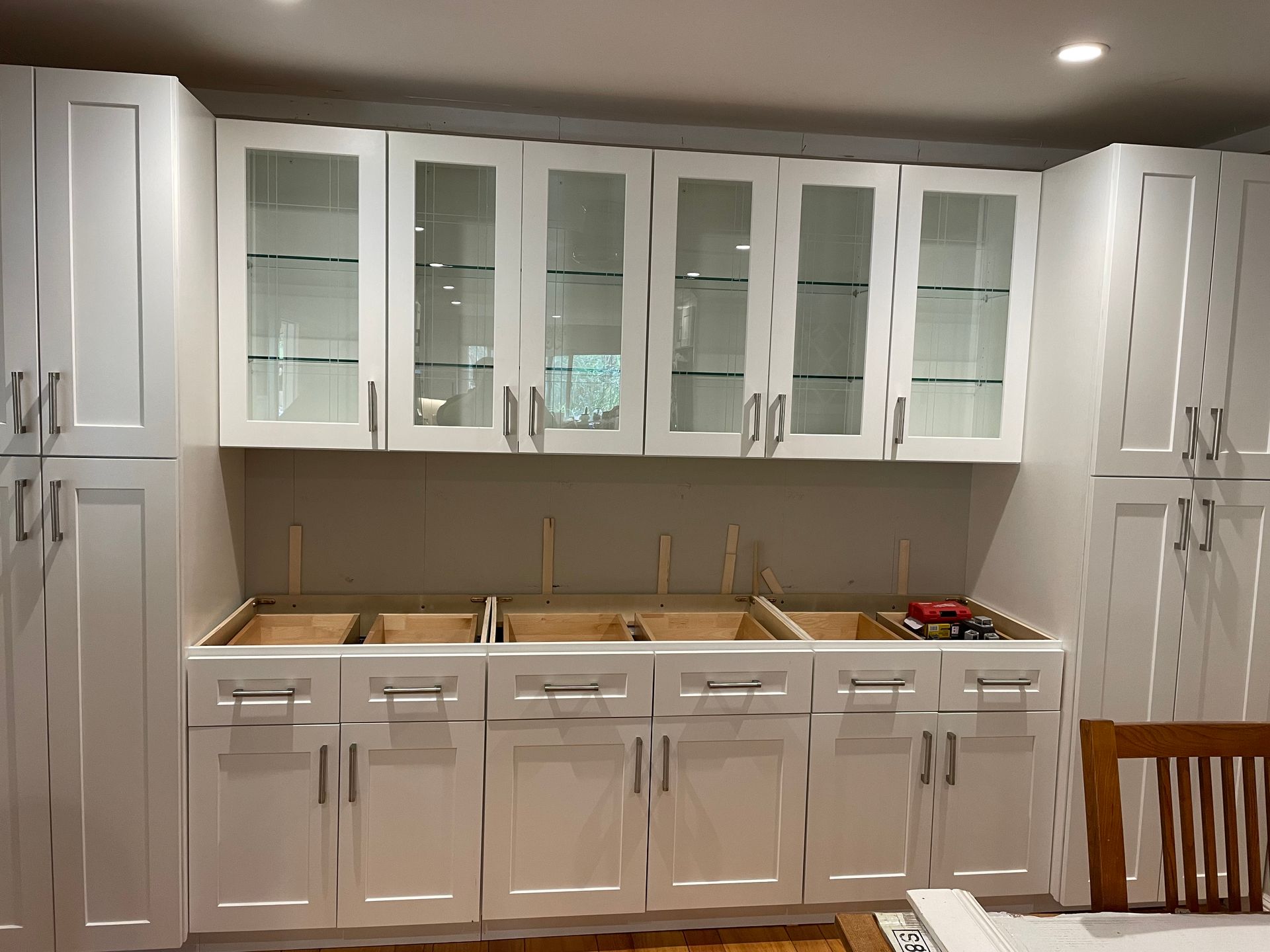 White kitchen wall with glass-front cabinets, white lower cabinets, and a tan backsplash under recessed lighting