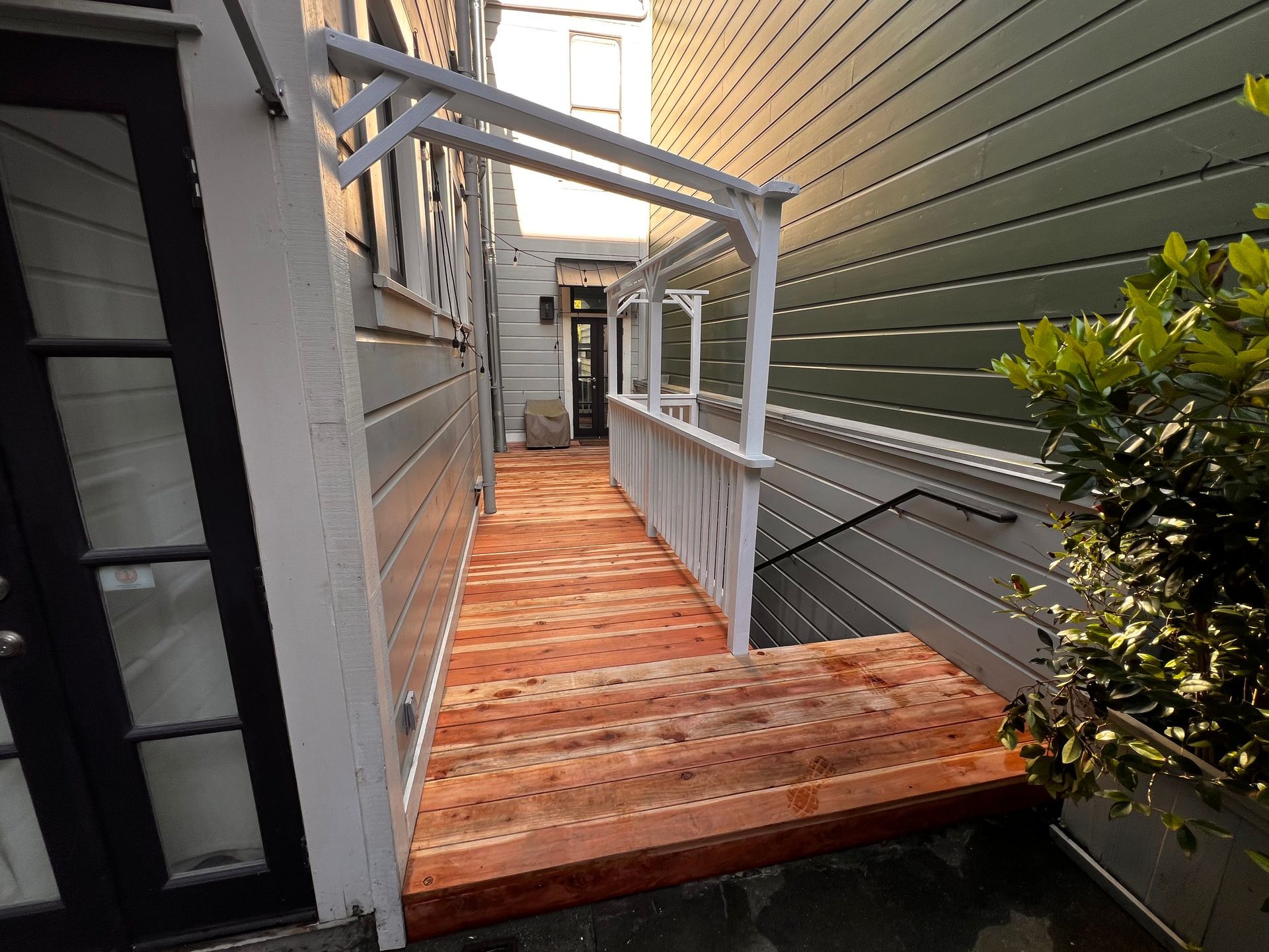 Wooden ramp between buildings with white railings and a black door at the end
