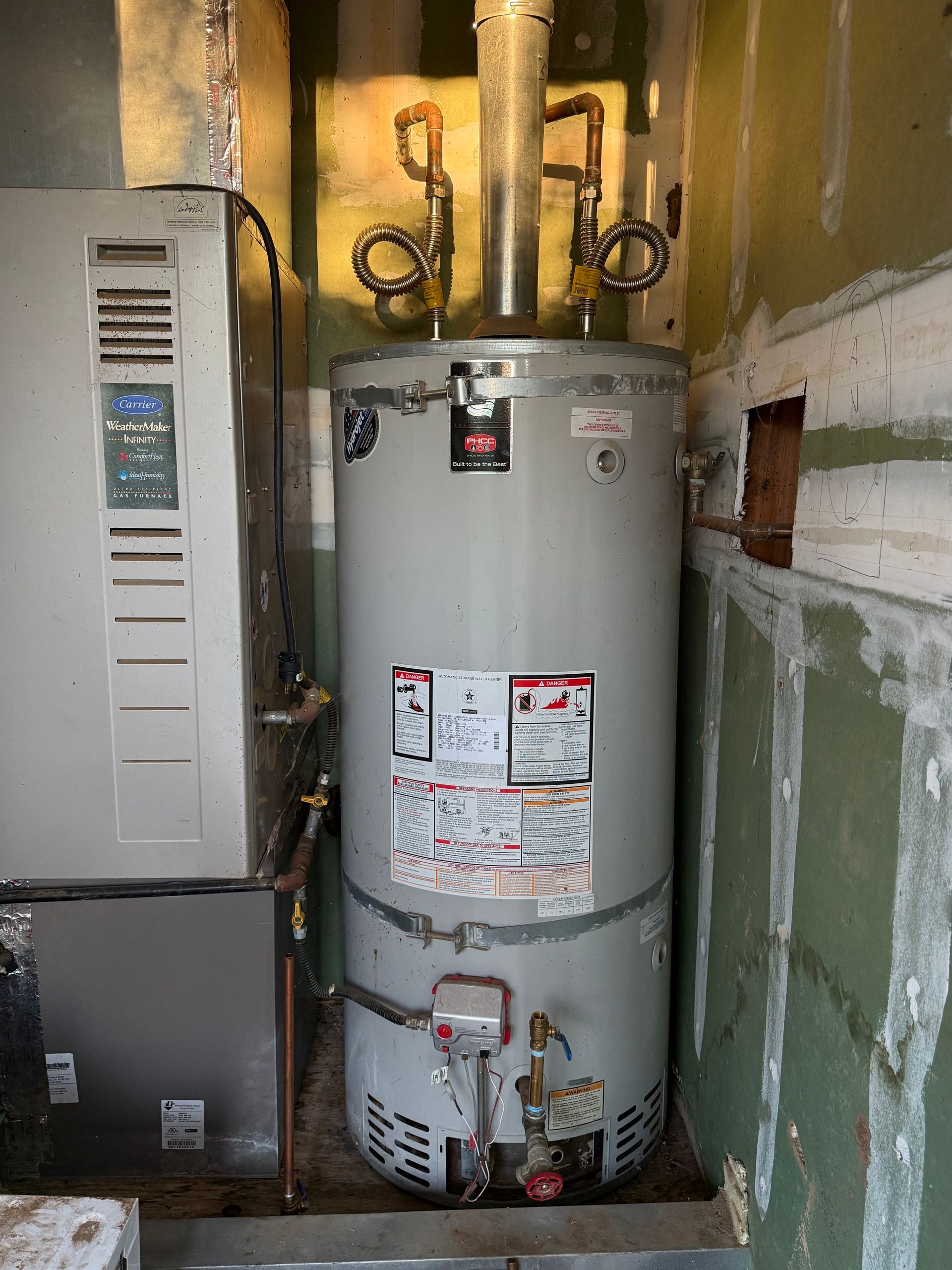 Water heater in a utility closet next to a furnace, with exposed pipes and venting.