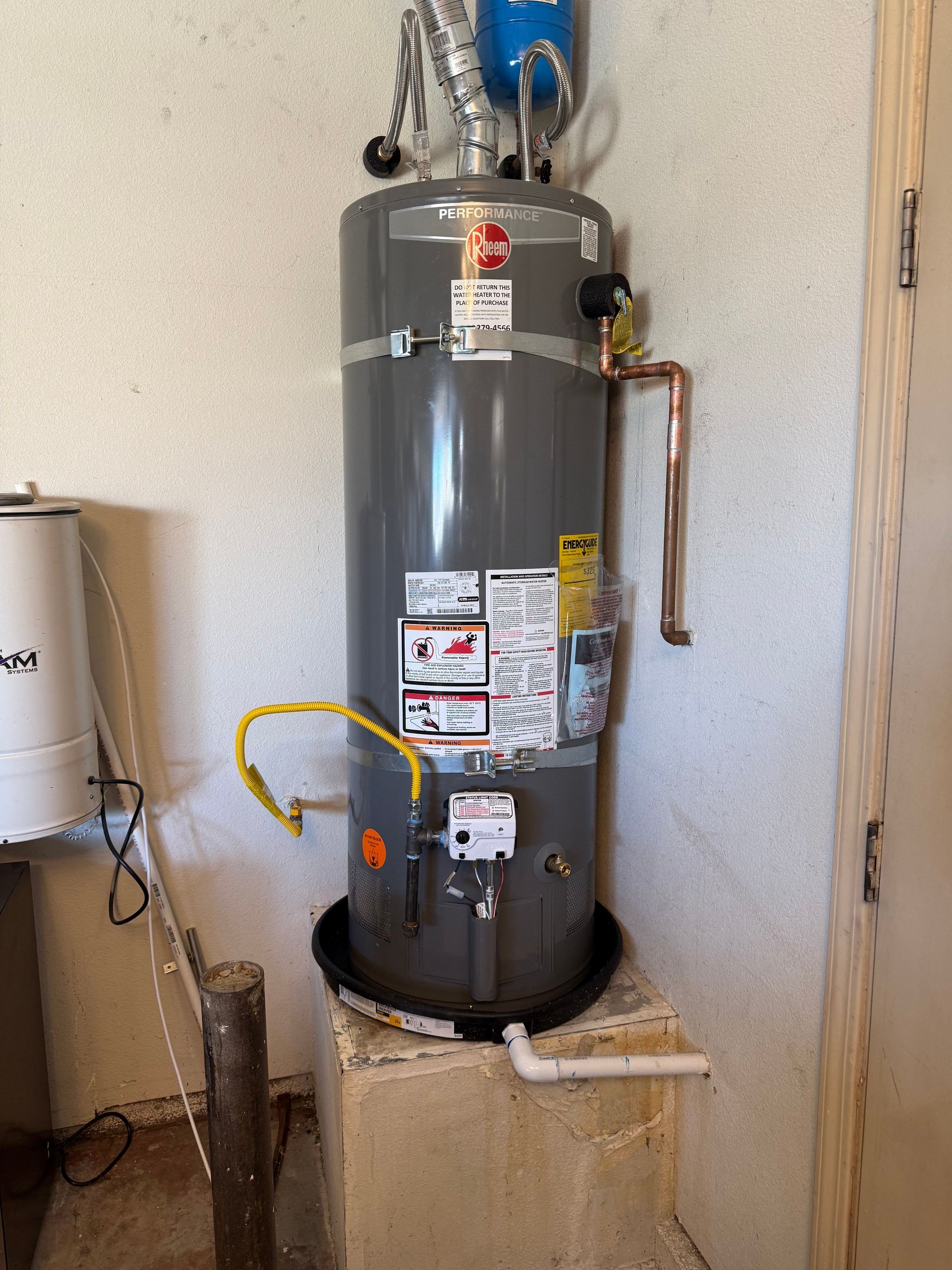 Gray water heater with pipes and labels in a small utility closet.