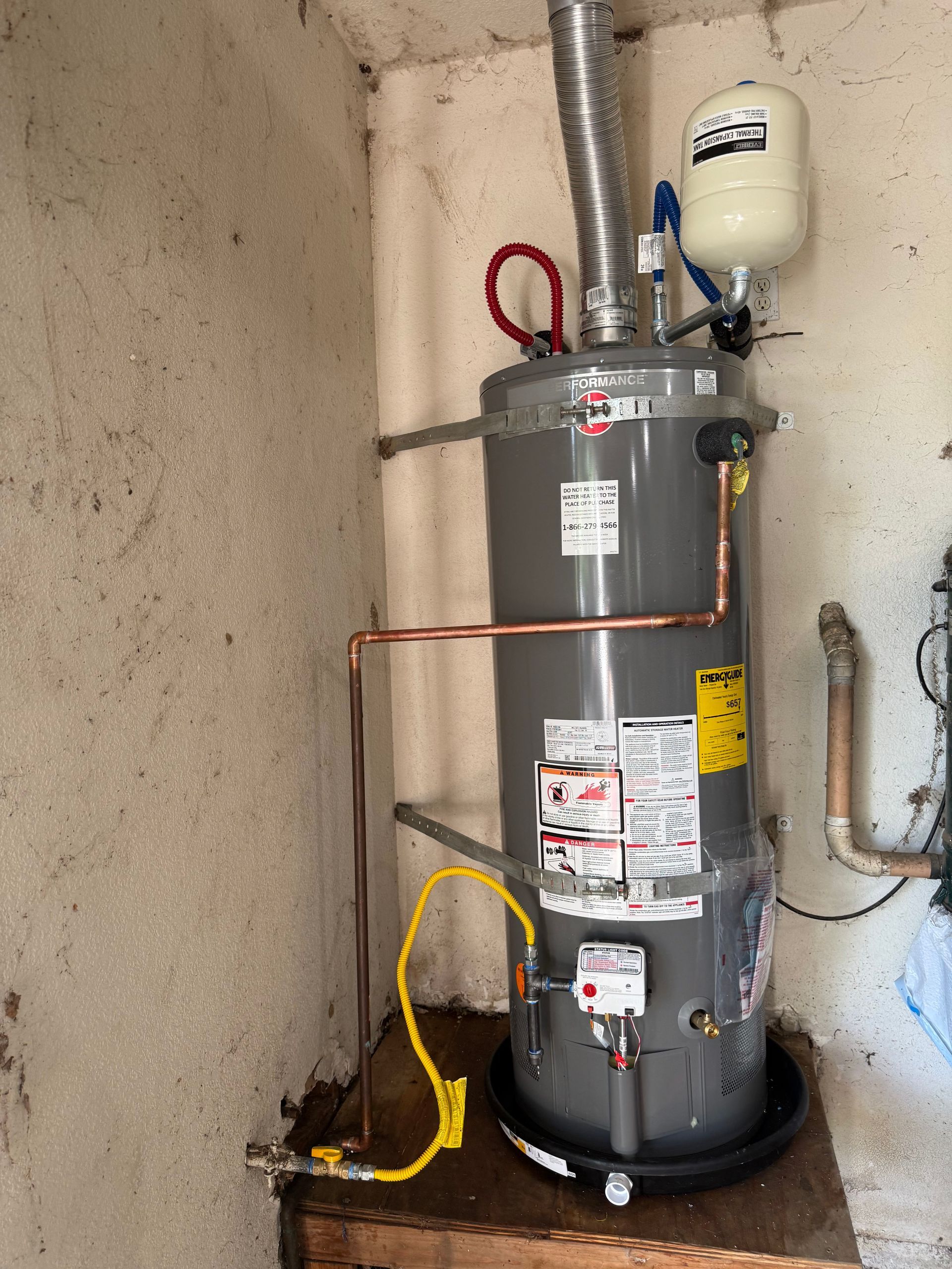 Gray water heater with copper piping and yellow cord in a utility closet against a concrete wall