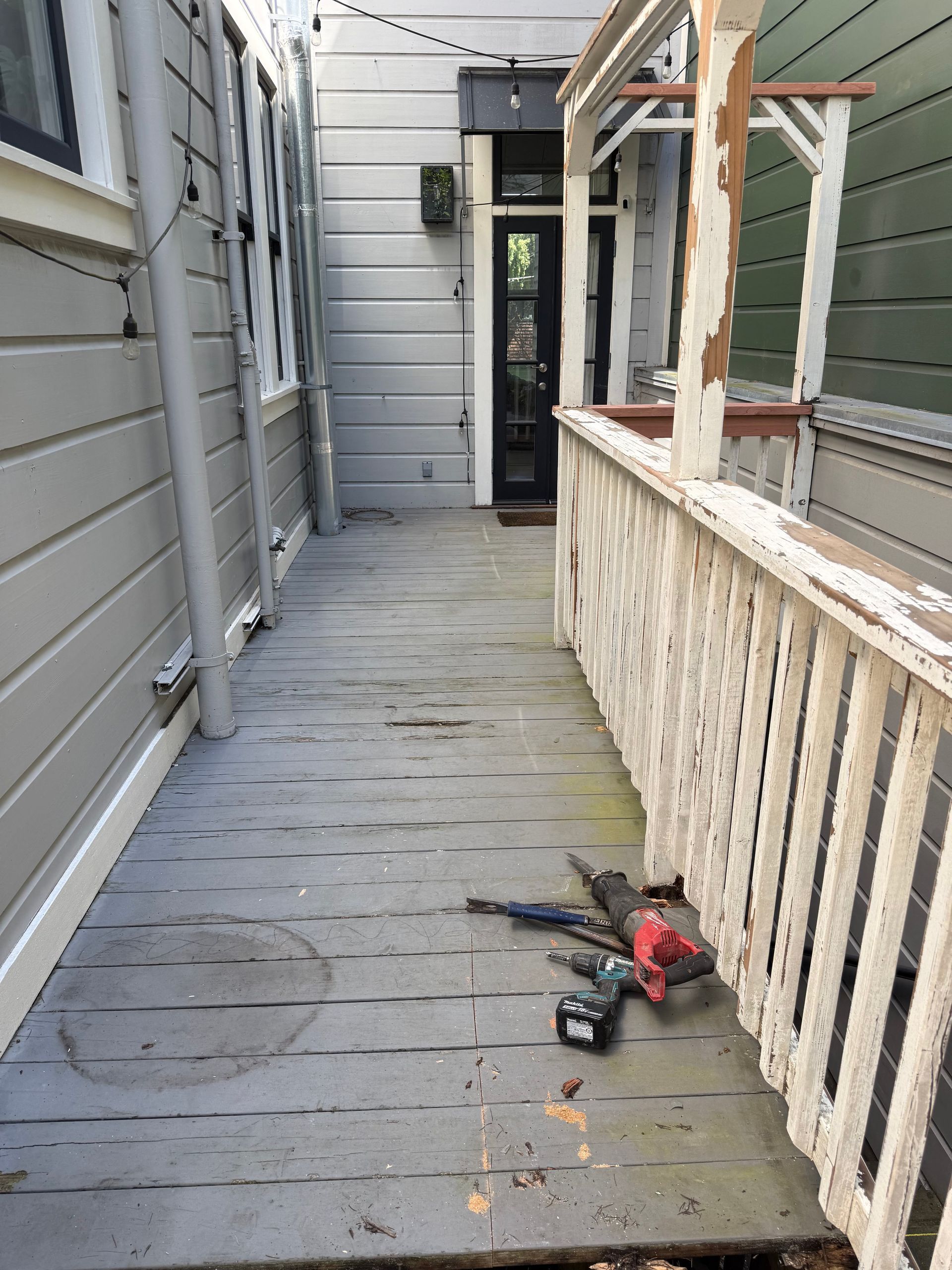 Narrow white-painted porch walkway with a drill and debris on the floor, leading to a front door.