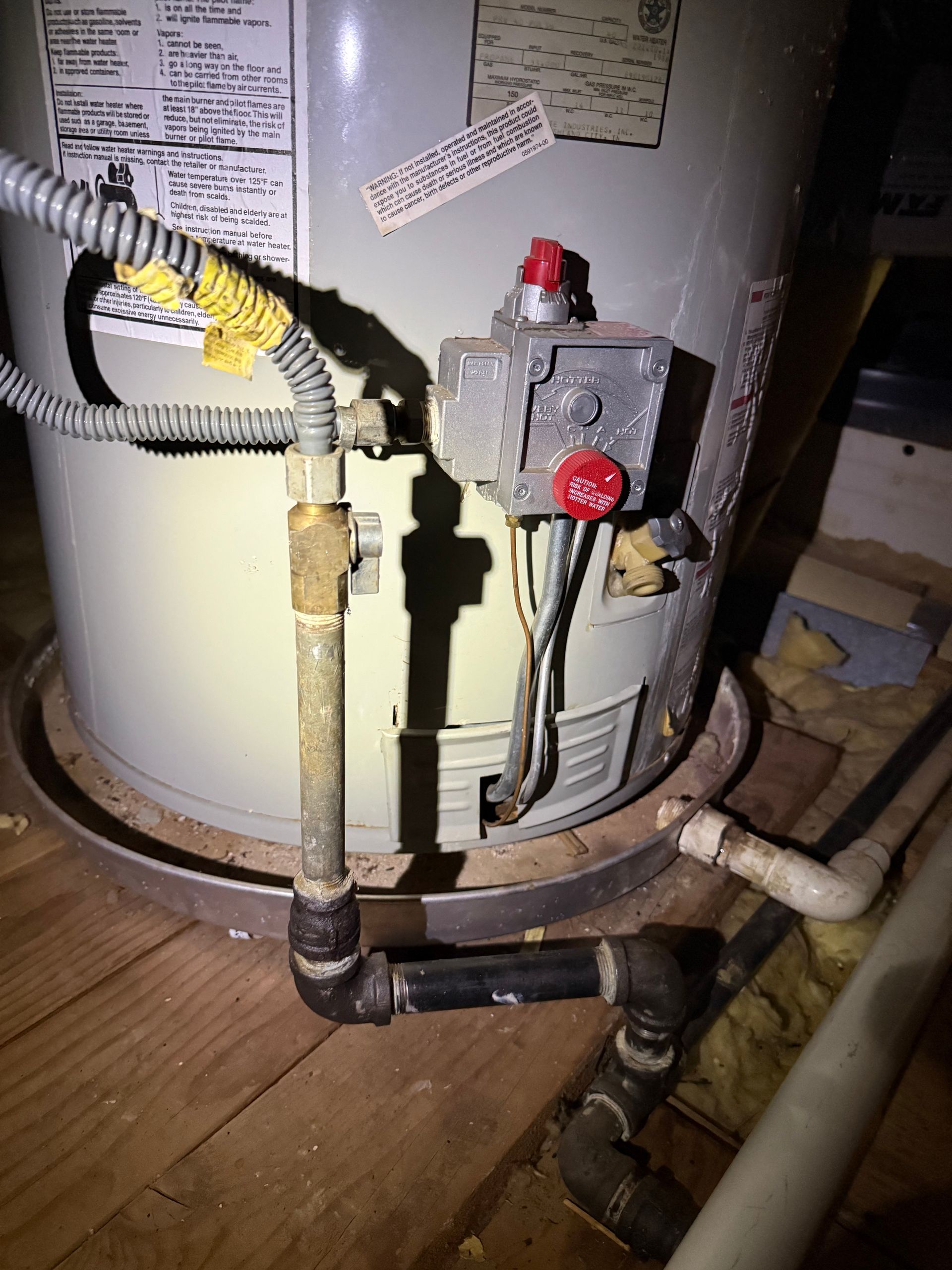 Gas water heater with control valve, red knob, and connected pipes in a basement or utility area