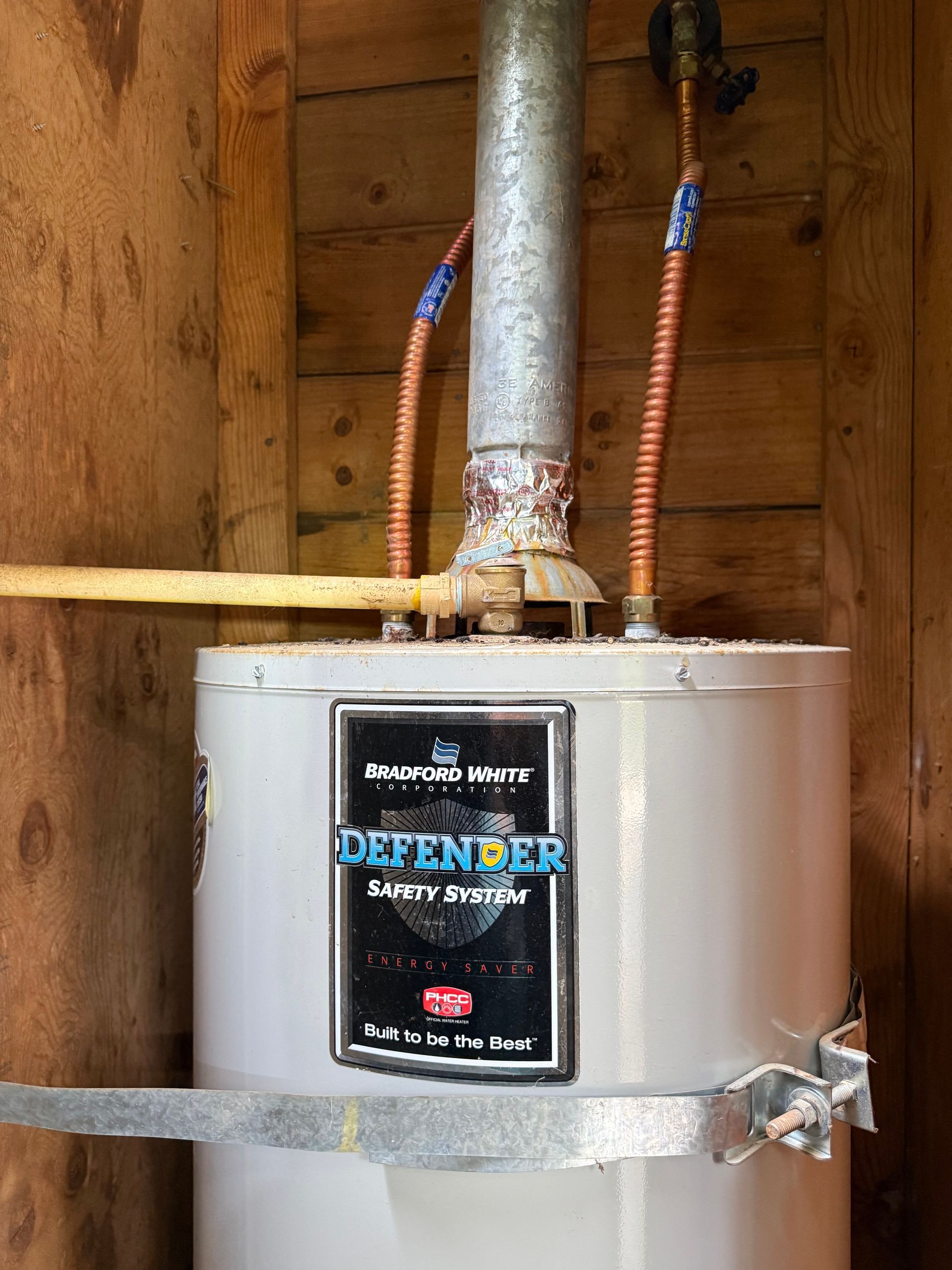 Water heater with a metal vent pipe and copper plumbing inside a wooden utility closet.