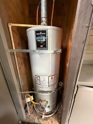 Water heater in a utility closet with exposed pipes and insulation on the sides.