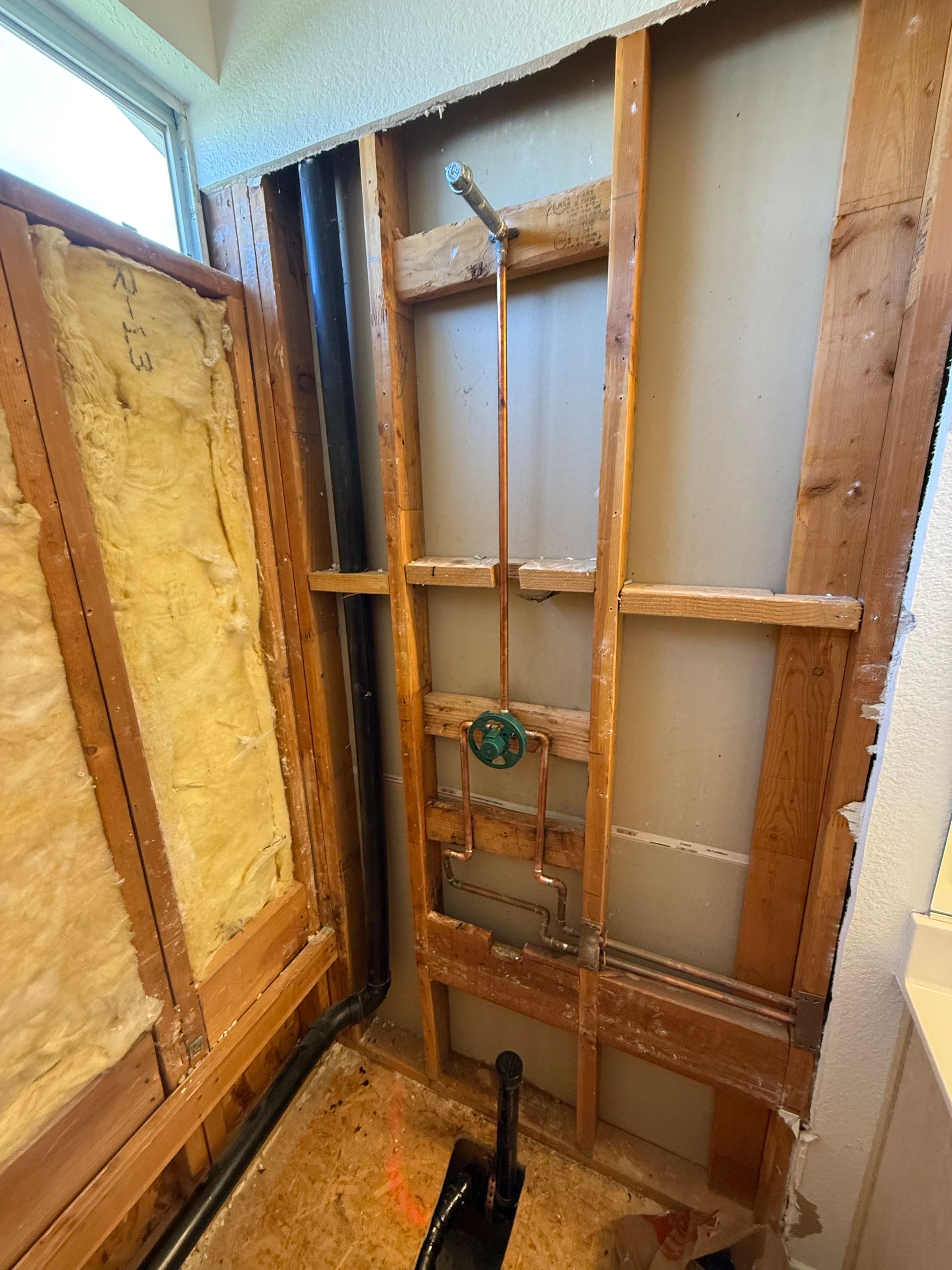 Open wall framing around a shower with exposed pipes, insulation, and plumbing fixtures.